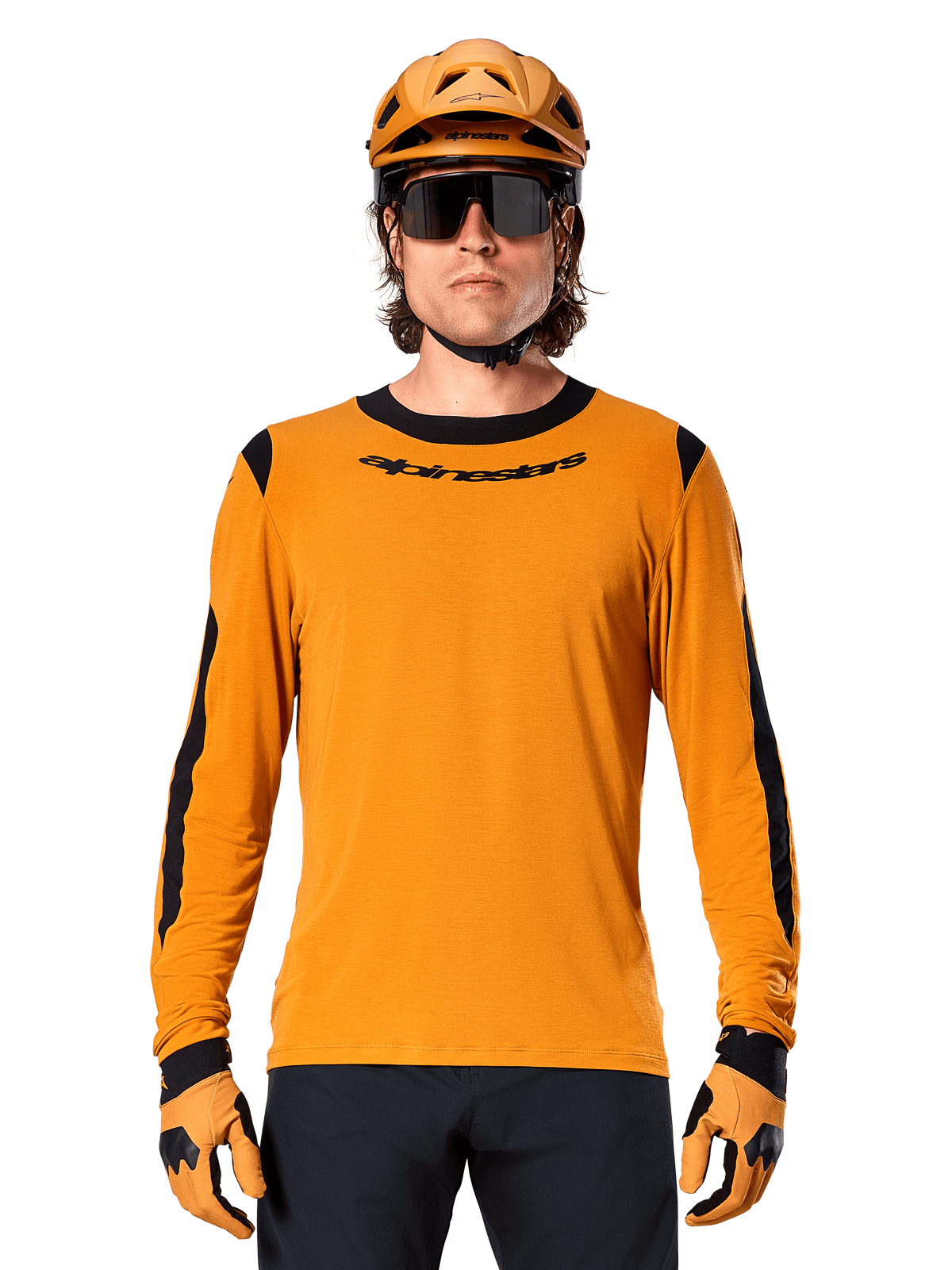 Modello che indossa la maglia a maniche lunghe Alpinestars A-Dura Dri Wool in Dark Gold, coordinata con casco da MTB e guanti oro abbinati, pannelli in rete nera su spalle e maniche, marchio Alpinestars nero sul petto, occhiali da sole e pantaloni scuri, abbigliamento tecnico da mountain bike