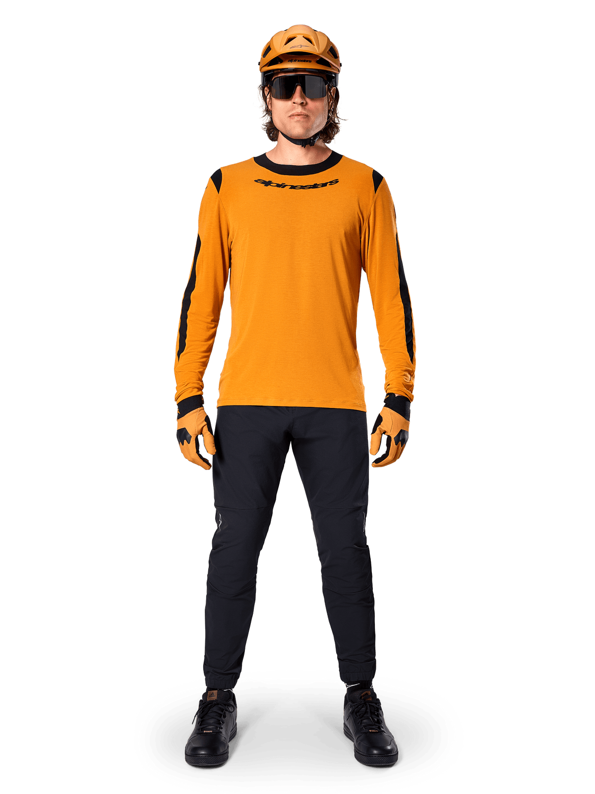 Mountain biker con maglia Alpinestars A-Dura Dri Wool a maniche lunghe, oro scuro con accenti neri su collo e maniche, abbinata a pantaloni neri, casco color oro coordinato, guanti e occhiali da sole neri, abbigliamento professionale da mountain bike