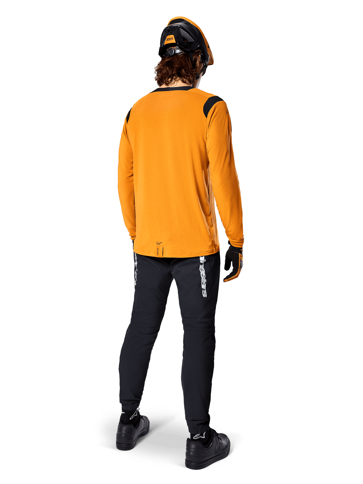 Mountain biker visto da dietro che indossa la maglia Alpinestars A-Dura Dri Wool a maniche lunghe in Dark Gold, pantaloni tecnici neri con logo bianco e un casco coordinato nero e arancione, abbigliamento da mountain bike ad alte prestazioni.