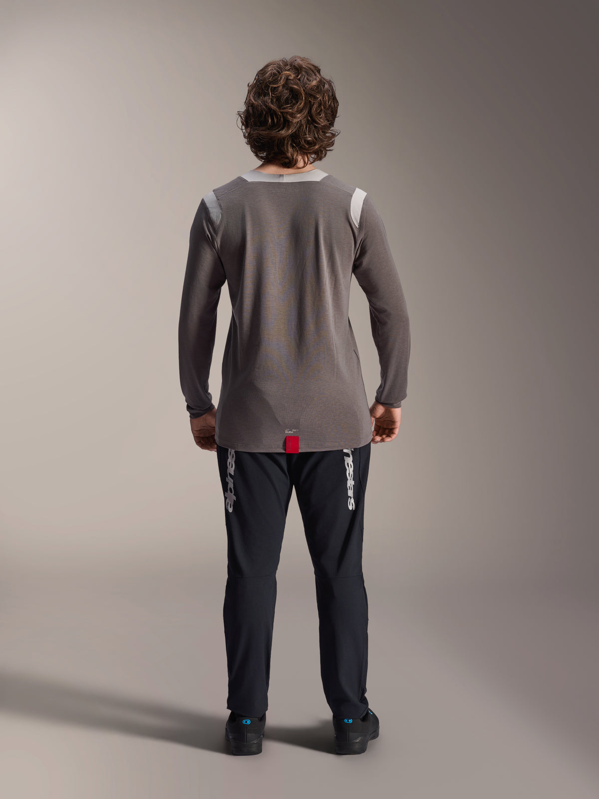 Pantaloni Alpinestars A-Dura Elite e maglia a maniche lunghe A-Dura Dri Wool, pantaloni neri con branding bianco, maglia tecnica grigia, vista posteriore dell'outfit da mountain bike, abbigliamento da ciclismo fuoristrada resistente