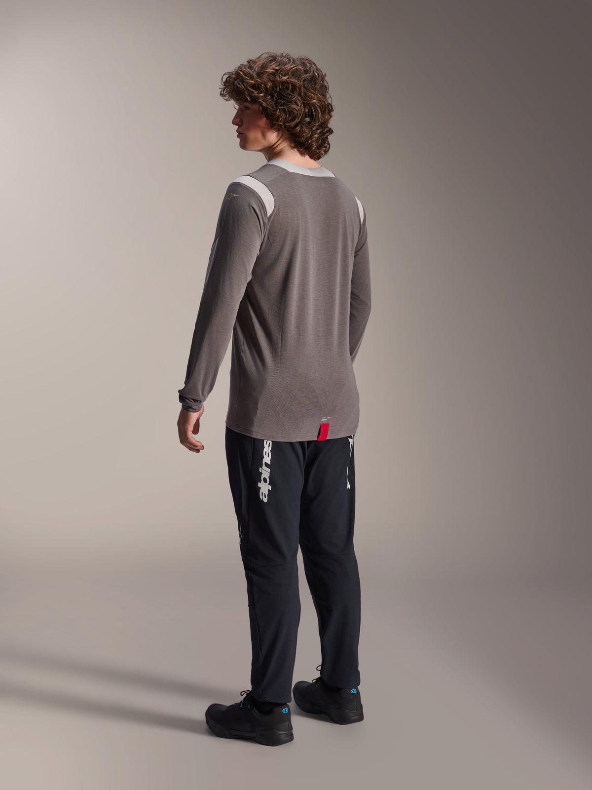 Maglia a maniche lunghe Alpinestars A-Dura Dri-Wool in grigio abbinata a pantaloni A-Dura Elite in nero, vista posteriore del modello, con logo Alpinestars bianco sulla gamba, abbigliamento tecnico da mountain bike per guida fuori strada