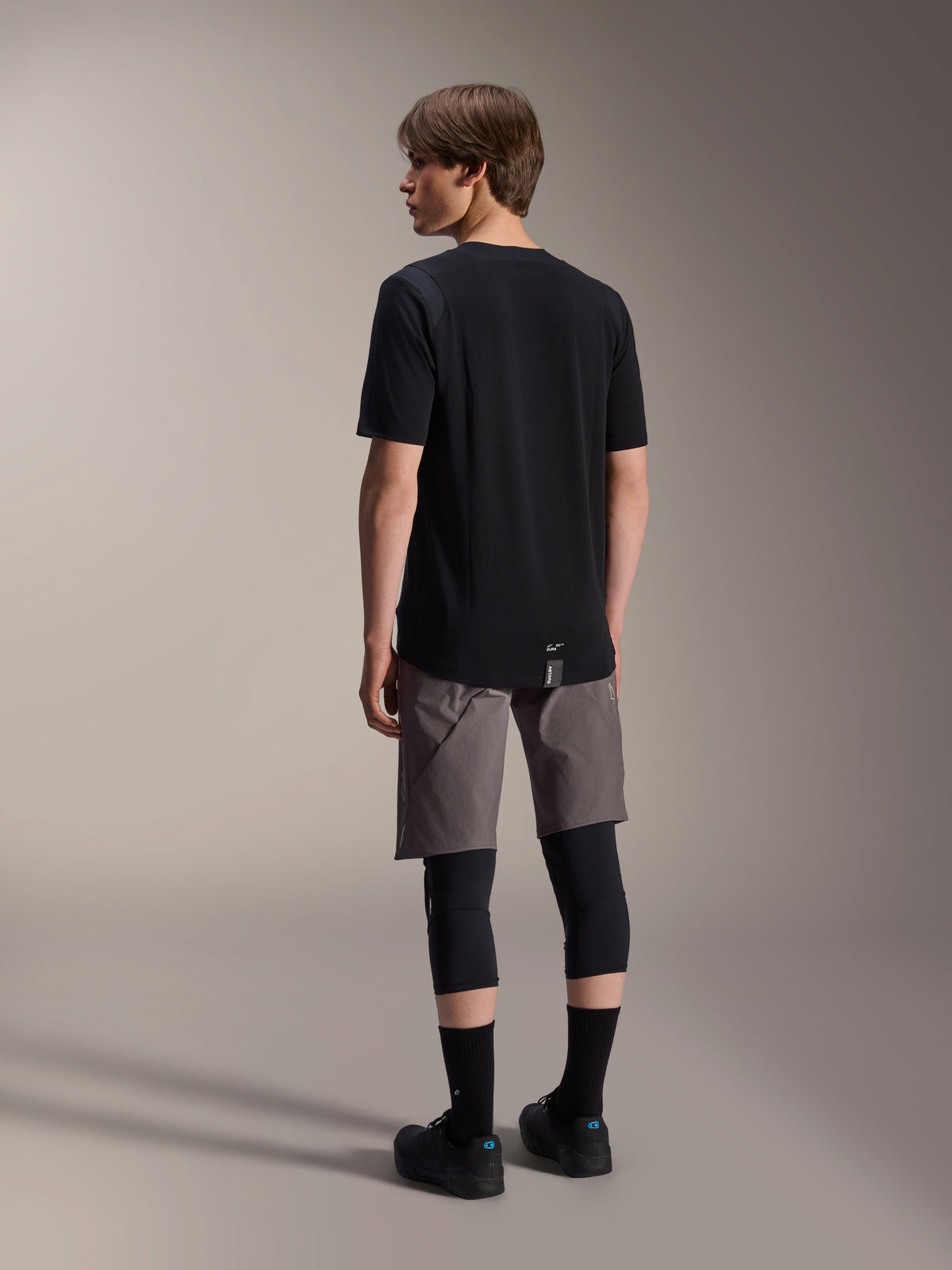 Maglia a maniche corte Alpinestars A-Dura Dri Wool e pantaloncini A-Dura Elite, abbigliamento da mountain bike nero e grigio scuro, indossati con ginocchiere e calze nere, vista posteriore dell'abbigliamento tecnico per prestazioni off-road