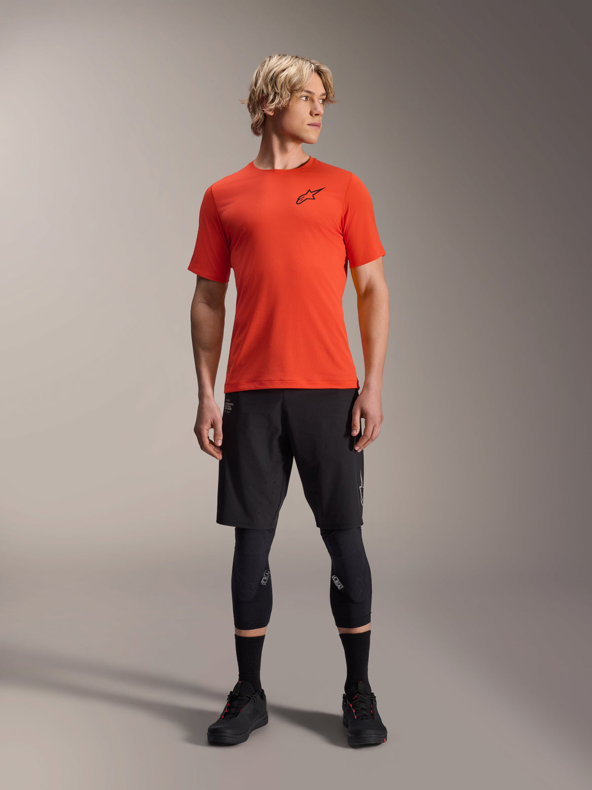 Maglia Alpinestars A-Aria Astar a maniche corte, Spicy Orange, indossata da un modello con pantaloncini neri da mountain bike e ginocchiere, abbigliamento tecnico da ciclismo leggero e traspirante per MTB