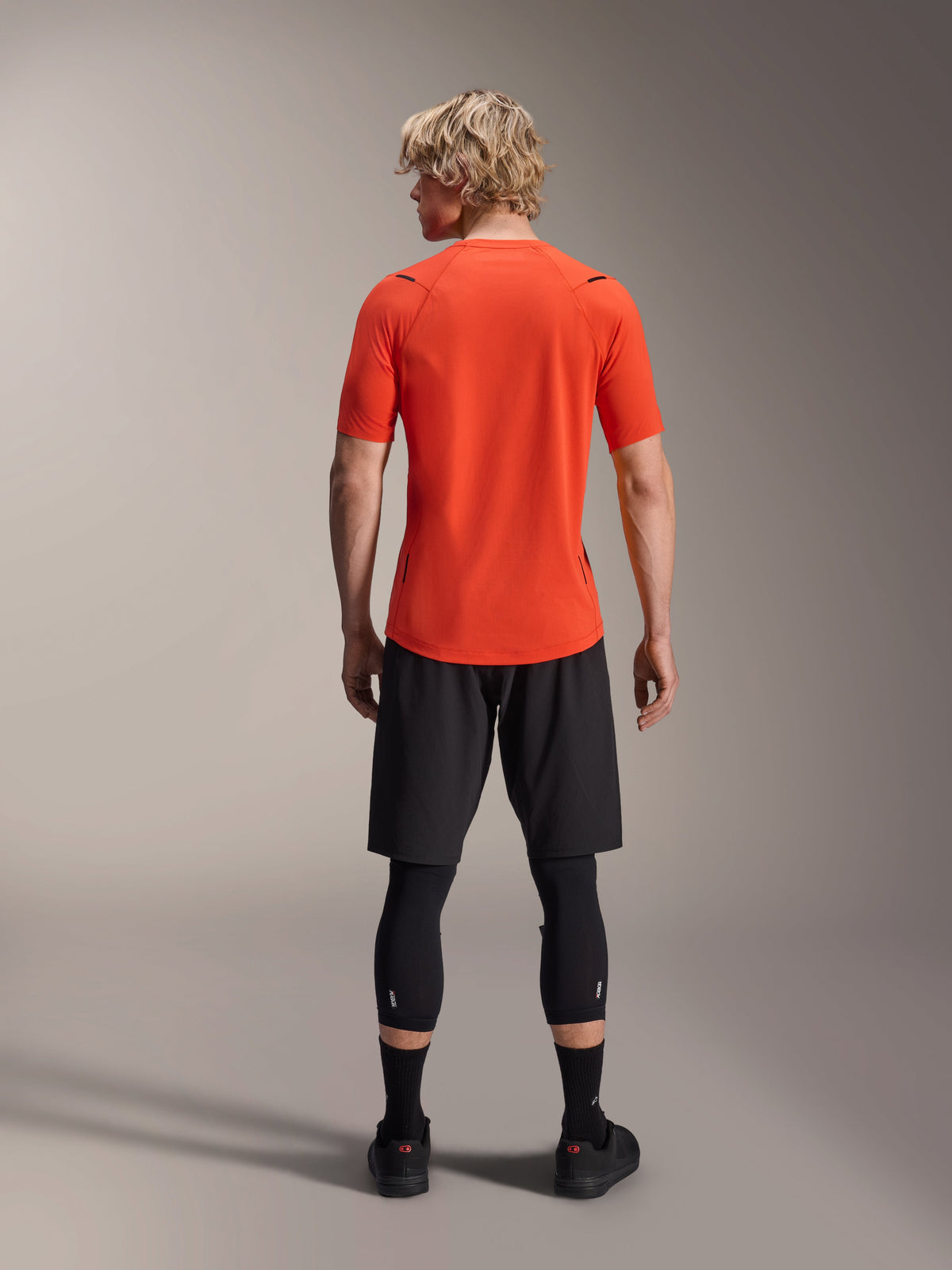 Alpinestars A-Aria Astar Jersey, maglia MTB a maniche corte, Spicy Orange, vista posteriore che mostra la vestibilità performante e la coda più lunga, abbinata a pantaloncini da ciclismo neri e leggings
