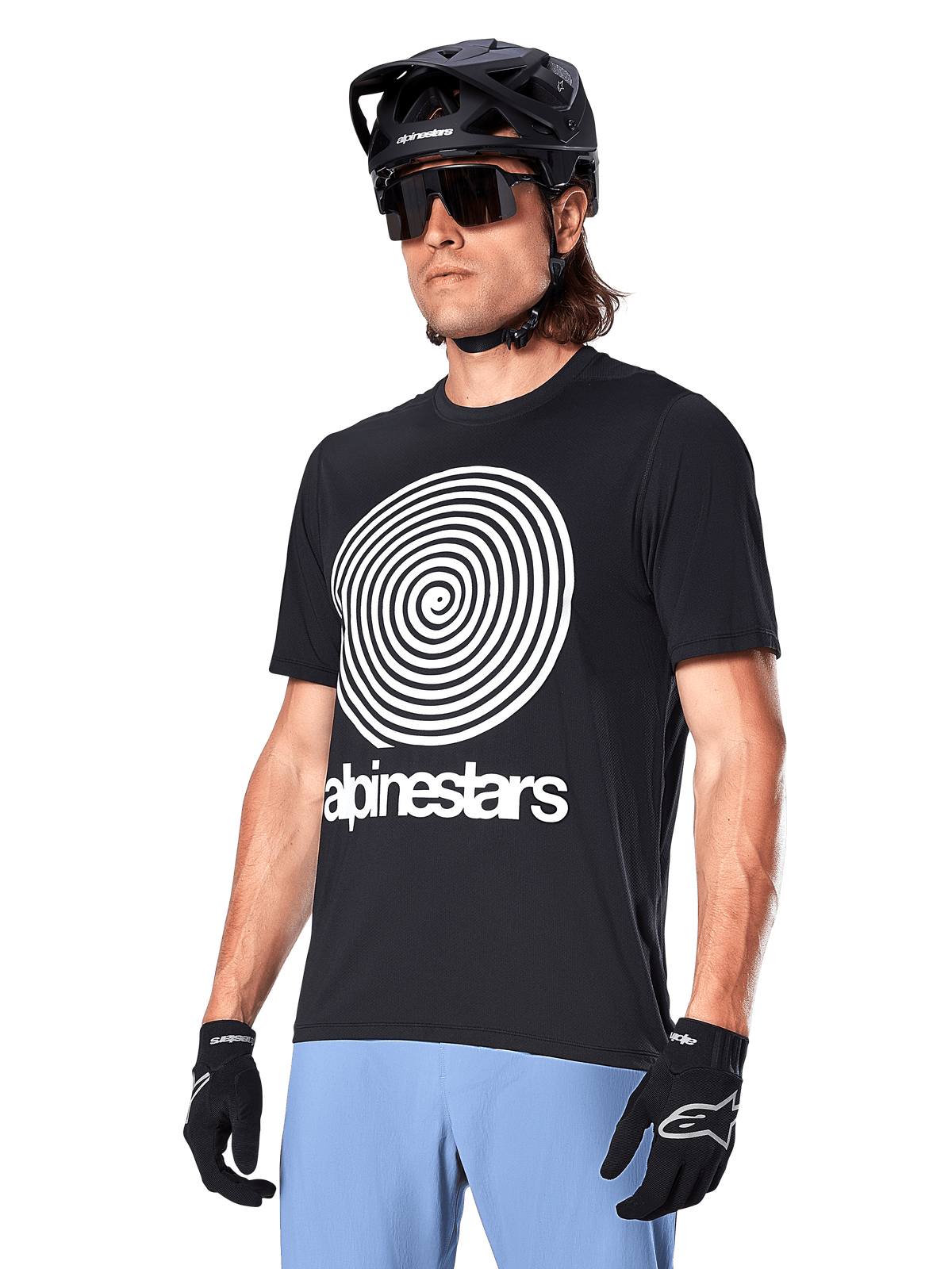 Alpinestars A-Dura Oscar Jersey - Manica Corta, nero, con grande grafica a spirale bianca e marchio Alpinestars sul petto, indossata da un ciclista con casco da MTB nero, occhiali da sole e pantaloni azzurri