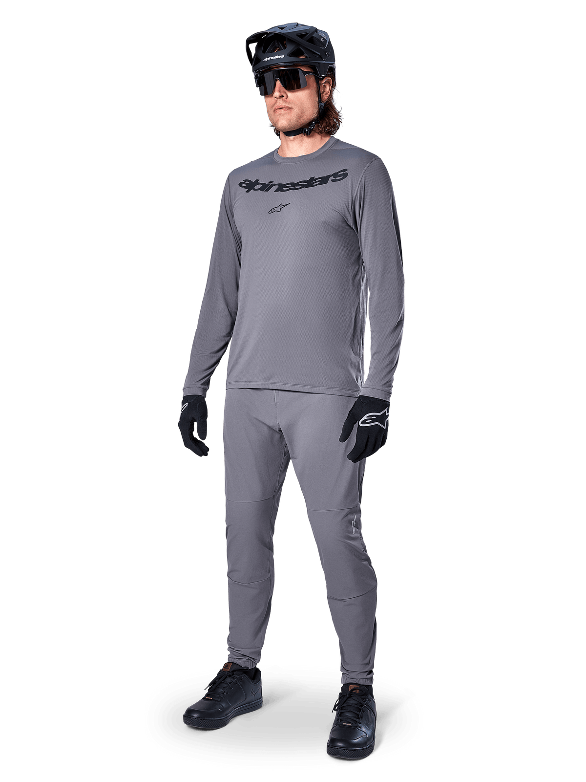 Alpinestars A-Dura Rocker Jersey - Maniche Lunghe, grigio scuro, indossata da un modello con pantaloni grigi coordinati, casco da mountain bike nero, occhiali da sole e guanti, stile casual MTB per la guida fuoristrada
