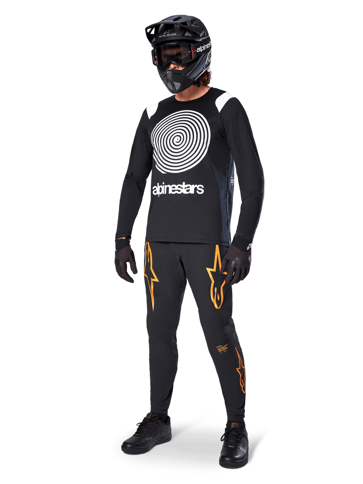 Pilota di MTB che indossa la maglia Alpinestars A-Supra Oscar a maniche lunghe nera, caratterizzata dalla grafica vintage a spirale Oscar bianca, pantaloni neri con loghi a stella arancioni, casco integrale nero con maschera e guanti neri, abbigliamento professionale da mountain bike