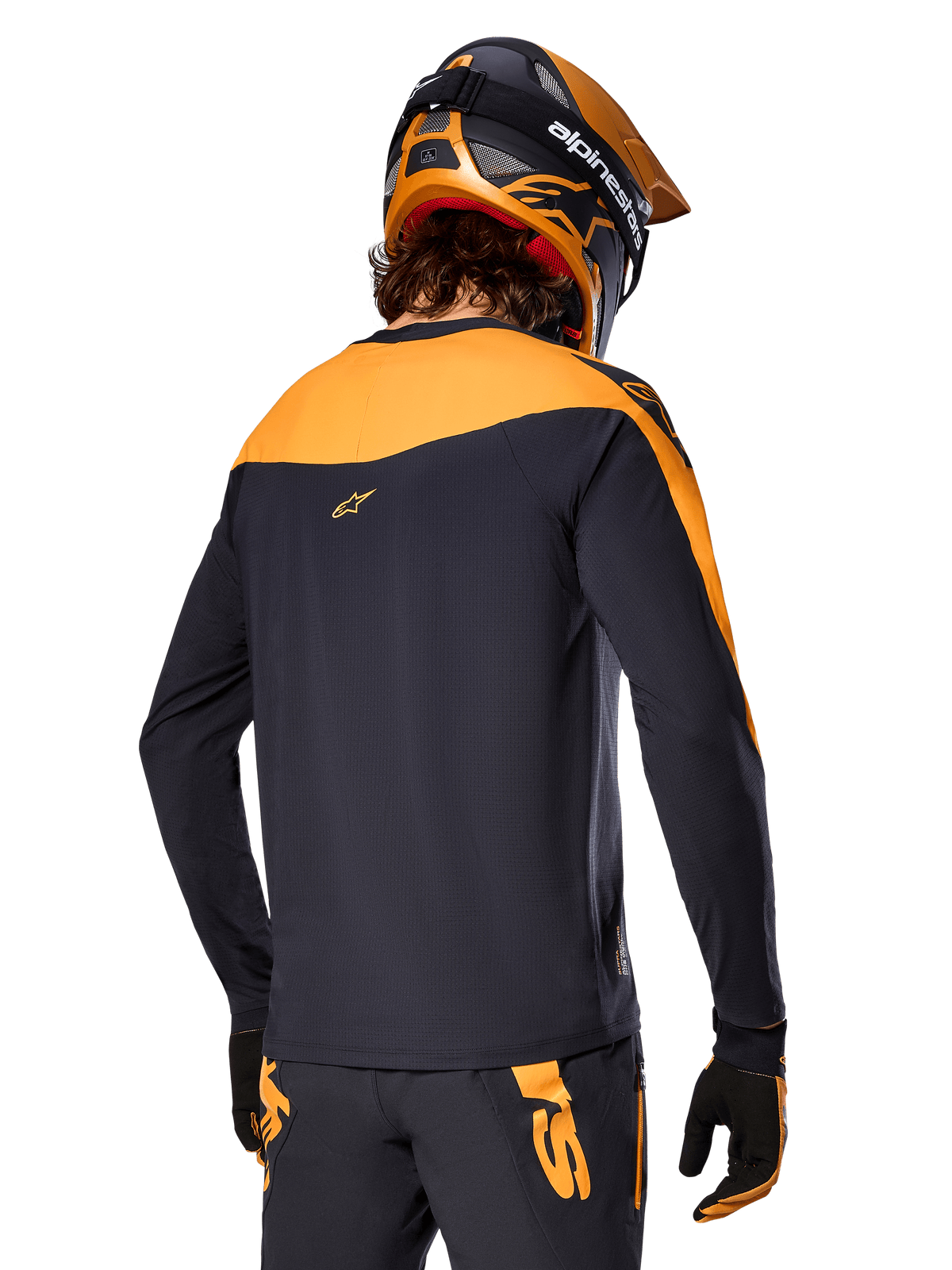 Alpinestars Maglia A-Supra Race - Maniche lunghe, nero e arancione, vista posteriore del pilota con casco e pantaloni da mountain bike coordinati, vestibilità performance con texture microperforata, abbigliamento professionale da gara MTB