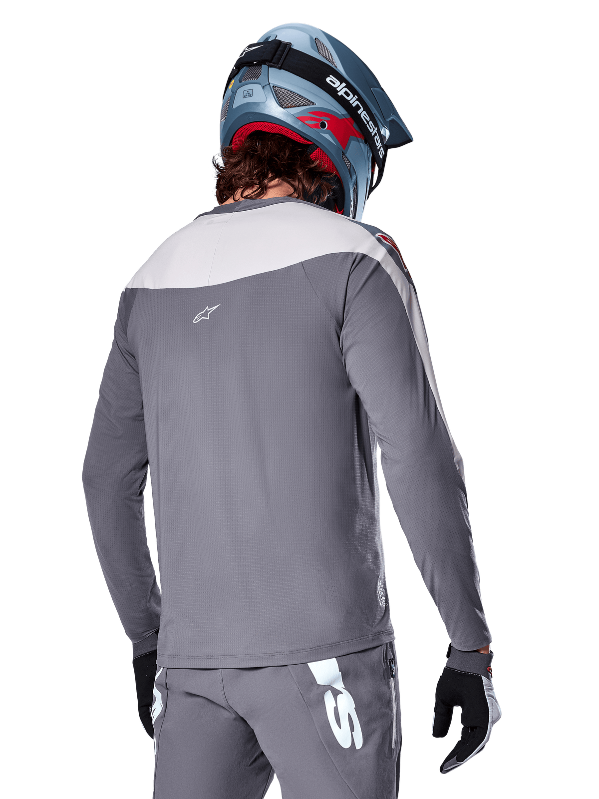Alpinestars A-Supra Race Jersey, maglia MTB a maniche lunghe in grigio scuro e grigio chiaro, vista posteriore che mostra la vestibilità performance e il logo Astar, indossata con pantaloni grigi coordinati e un casco da mountain bike blu, progettata per il mountain bike fuoristrada.