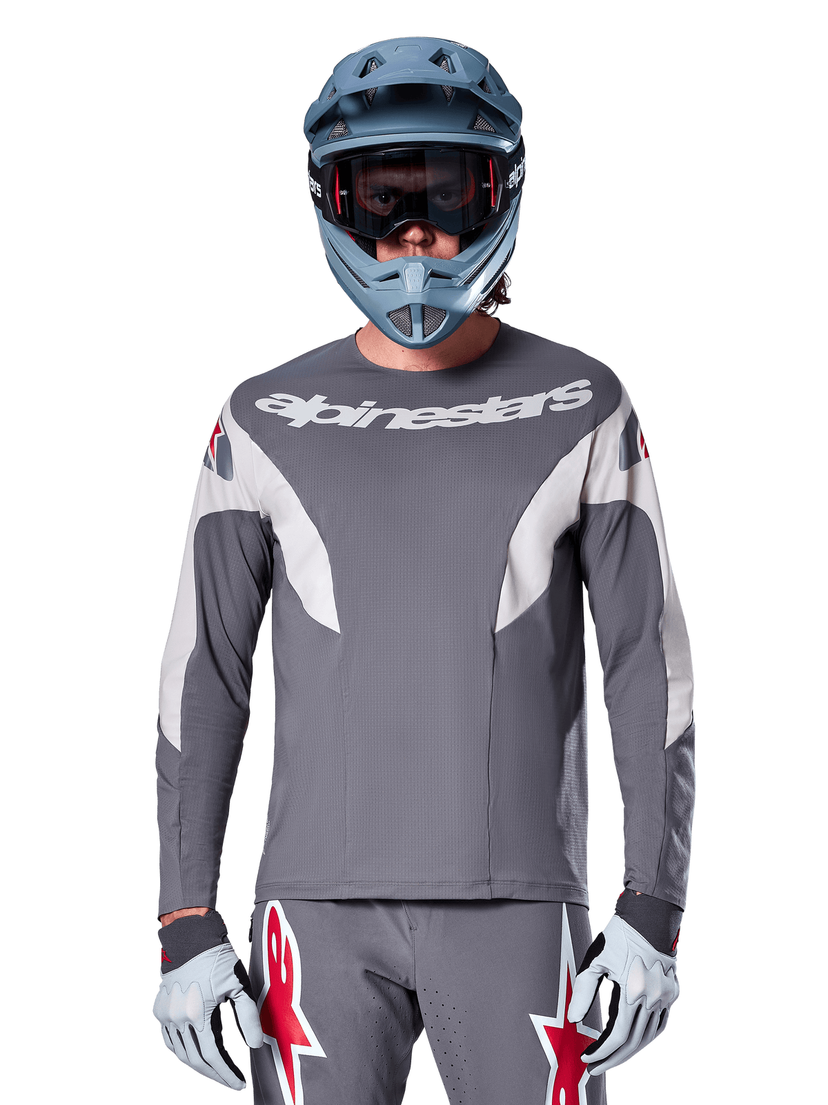 Ciclista MTB che indossa la maglia Alpinestars A-Supra Race - Manica Lunga in grigio scuro, maglia da ciclismo a maniche lunghe con logo Alpinestars bianco, abbinata a casco integrale grigio-azzurro, maschera e guanti da corsa grigi, equipaggiamento completo da gara per mountain bike per prestazioni off-road