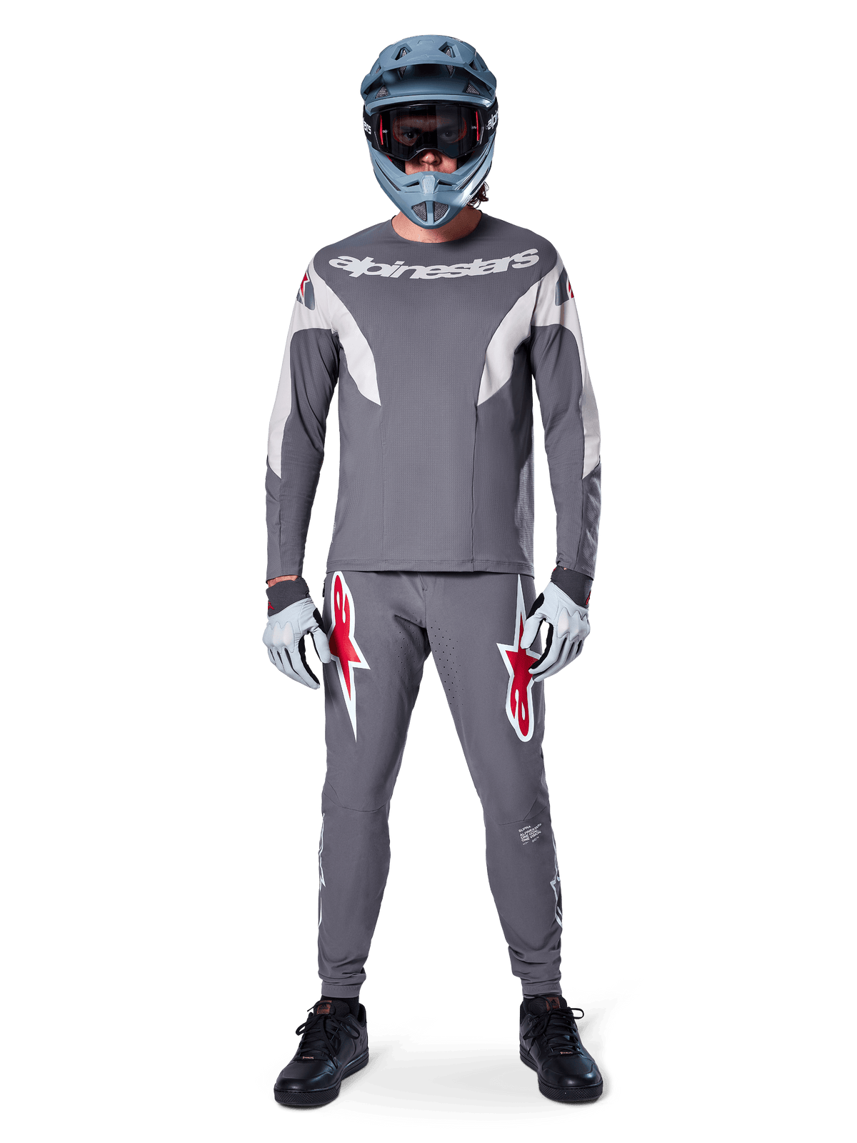 Rider con maglia Alpinestars A-Supra Race - Manica lunga in grigio scuro, coordinata con pantaloni grigi abbinati con vistosi loghi a stella rossi, casco grigio con maschera e guanti grigio chiaro, kit da gara MTB completo per il ciclismo fuoristrada ad alte prestazioni
