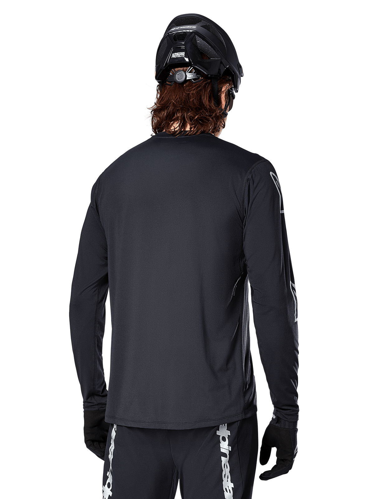 Maglia a maniche lunghe Alpinestars A-Dura Switch, nera, vista posteriore su un ciclista con casco MTB nero e guanti, in tessuto tecnico jacquard e con coda allungata per il fuoristrada