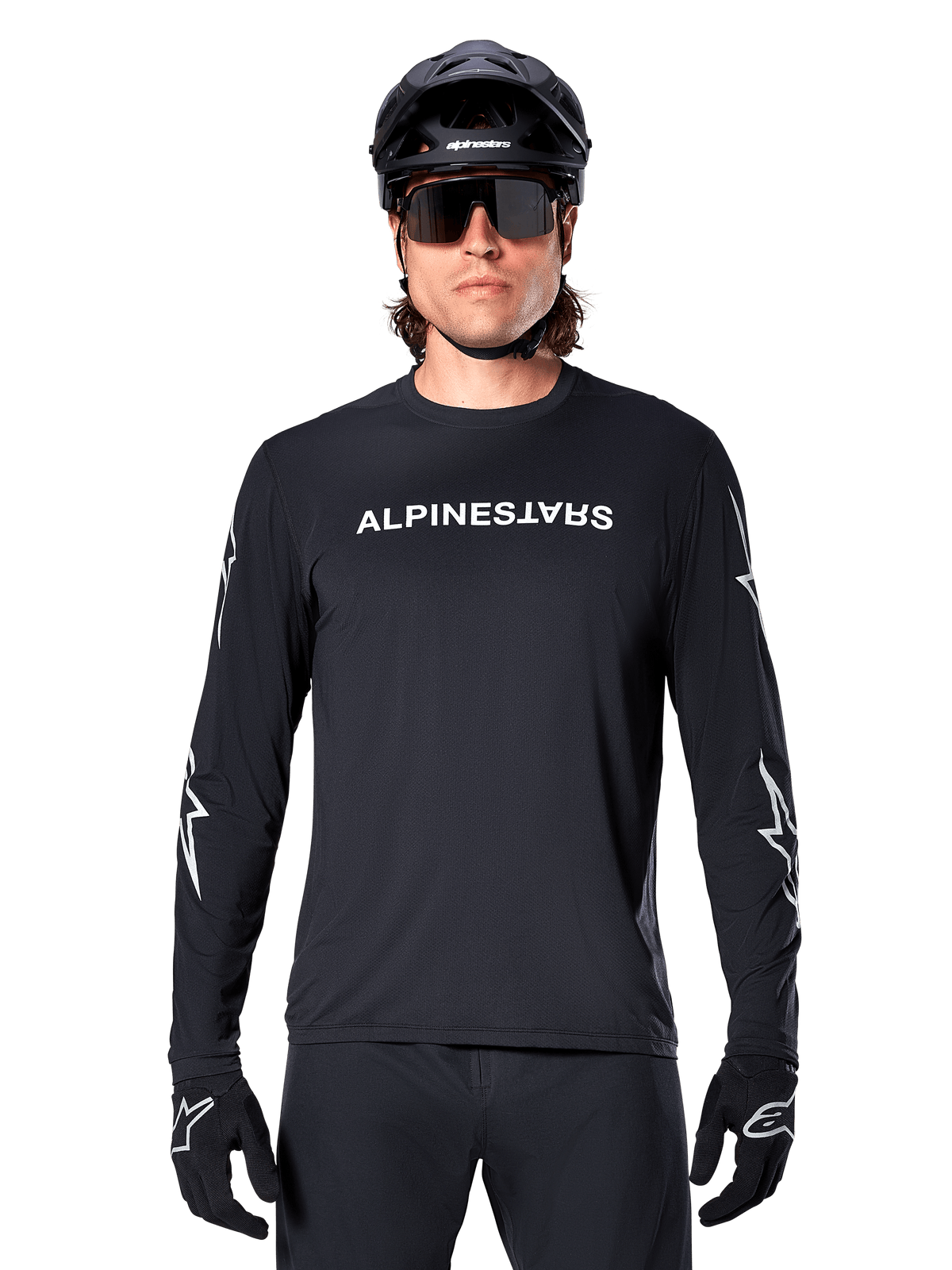 Alpinestars Maglia A-Dura Switch a maniche lunghe, maglia da MTB nera, scritta Alpinestars bianca sul petto e grafiche a stella sulle maniche, indossata con casco da mountain bike nero e occhiali tecnici, abbigliamento tecnico da trail