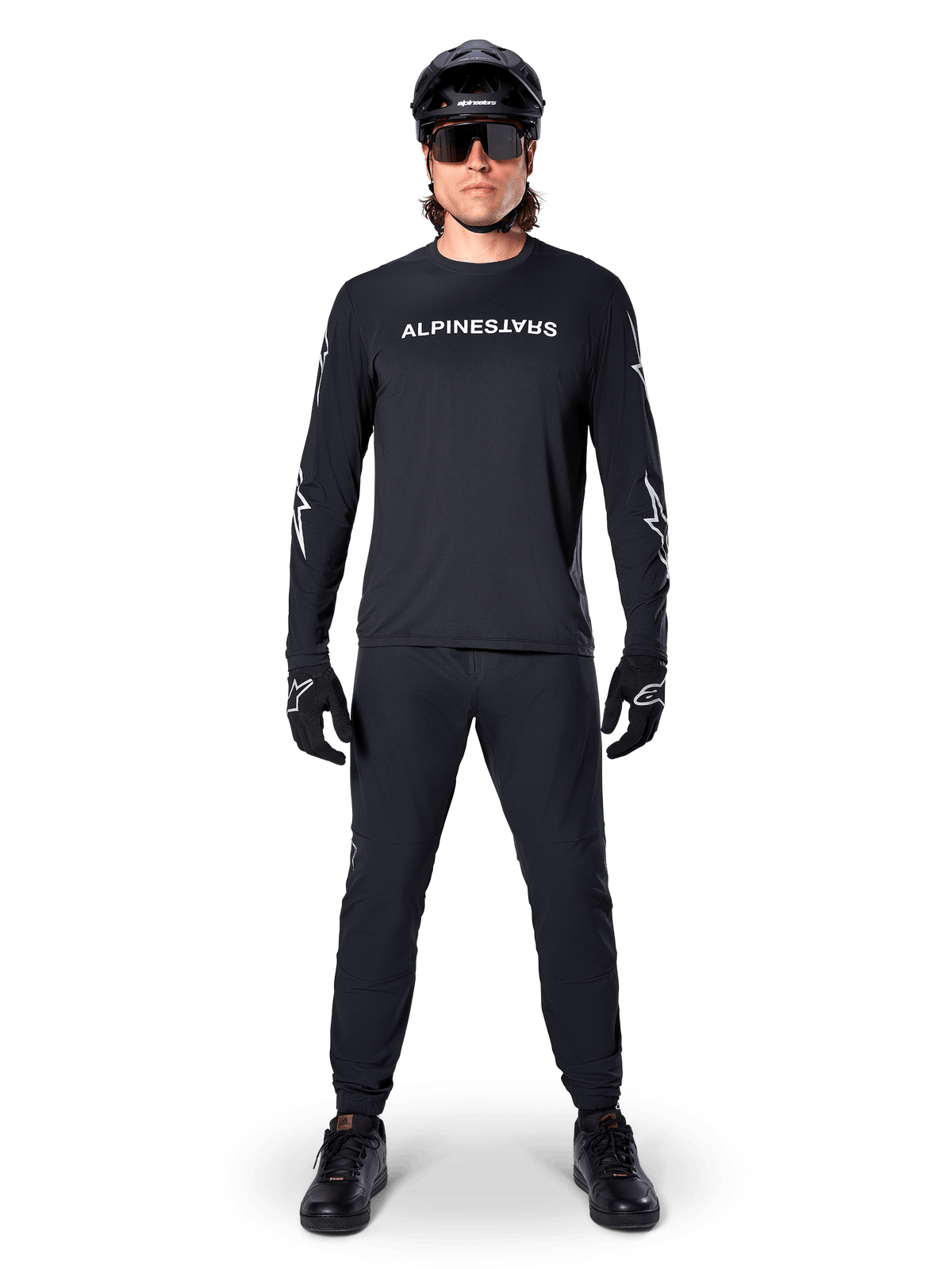 Maglia Alpinestars A-Dura Switch a maniche lunghe, nero, indossata da un ciclista di mountain bike con pantaloni e casco neri coordinati, con logo wordmark bianco sul petto, abbigliamento tecnico per ciclismo fuoristrada
