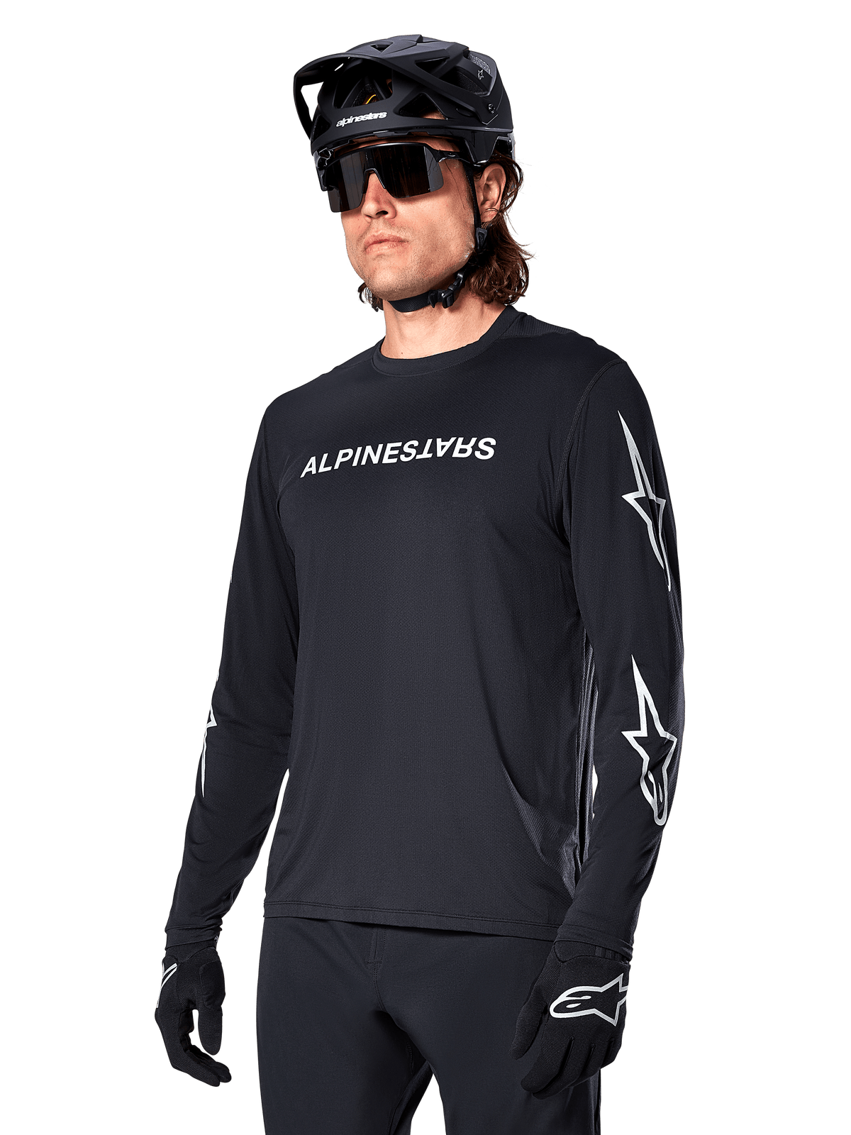Ciclista uomo che indossa la maglia a maniche lunghe Alpinestars A-Dura Switch, nero con scritta bianca e loghi a stella sulle maniche, abbinata a casco MTB nero e occhiali da sole, abbigliamento da ciclismo ad alte prestazioni per la guida fuoristrada