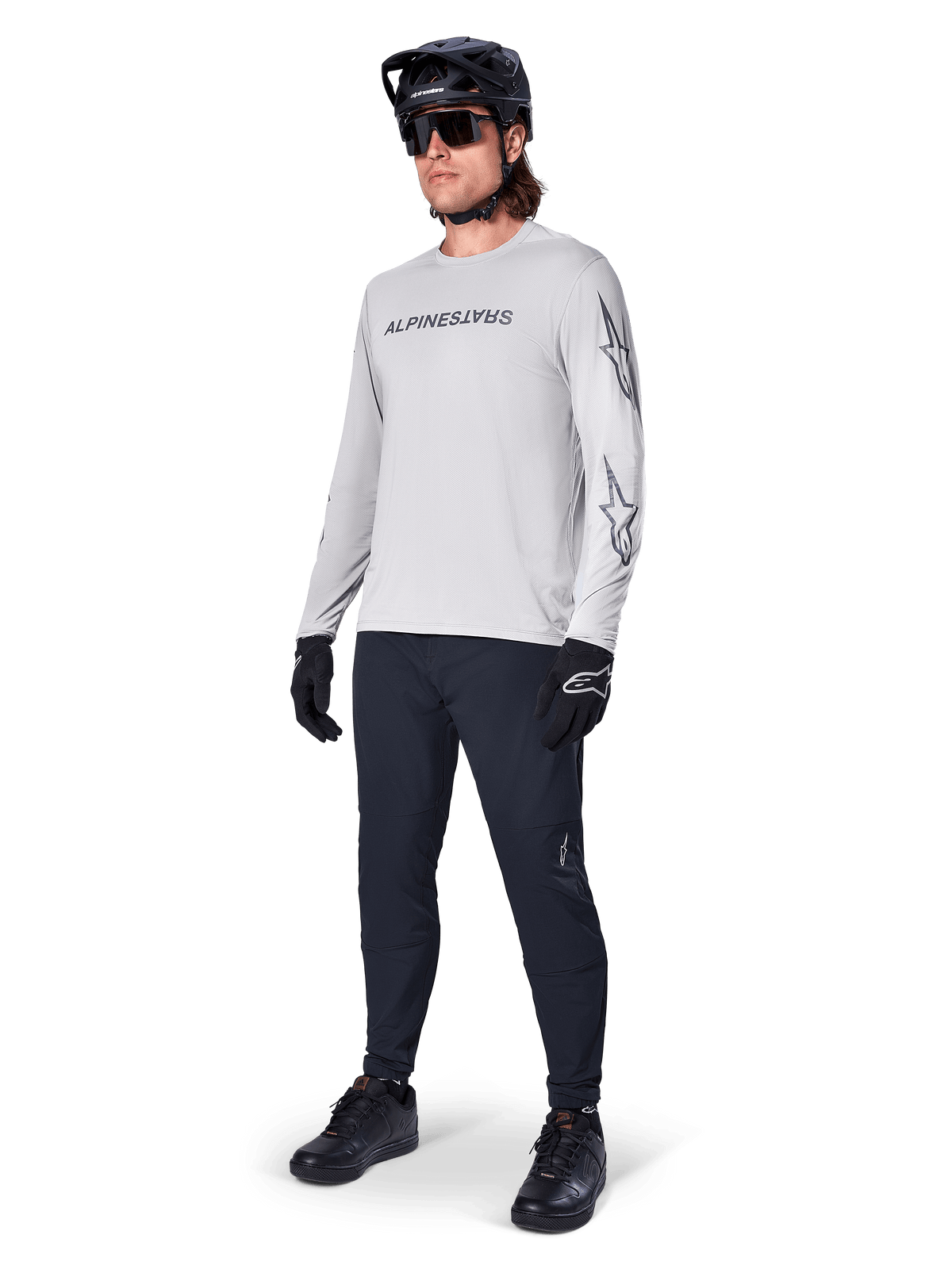 Maglia a maniche lunghe Alpinestars A-Dura Switch, Grigio Chiaro, indossata da un ciclista con pantaloni da mountain bike neri e casco, con logo wordmark nero sul petto e grafiche a stella sulle maniche, abbigliamento tecnico per ciclismo fuoristrada