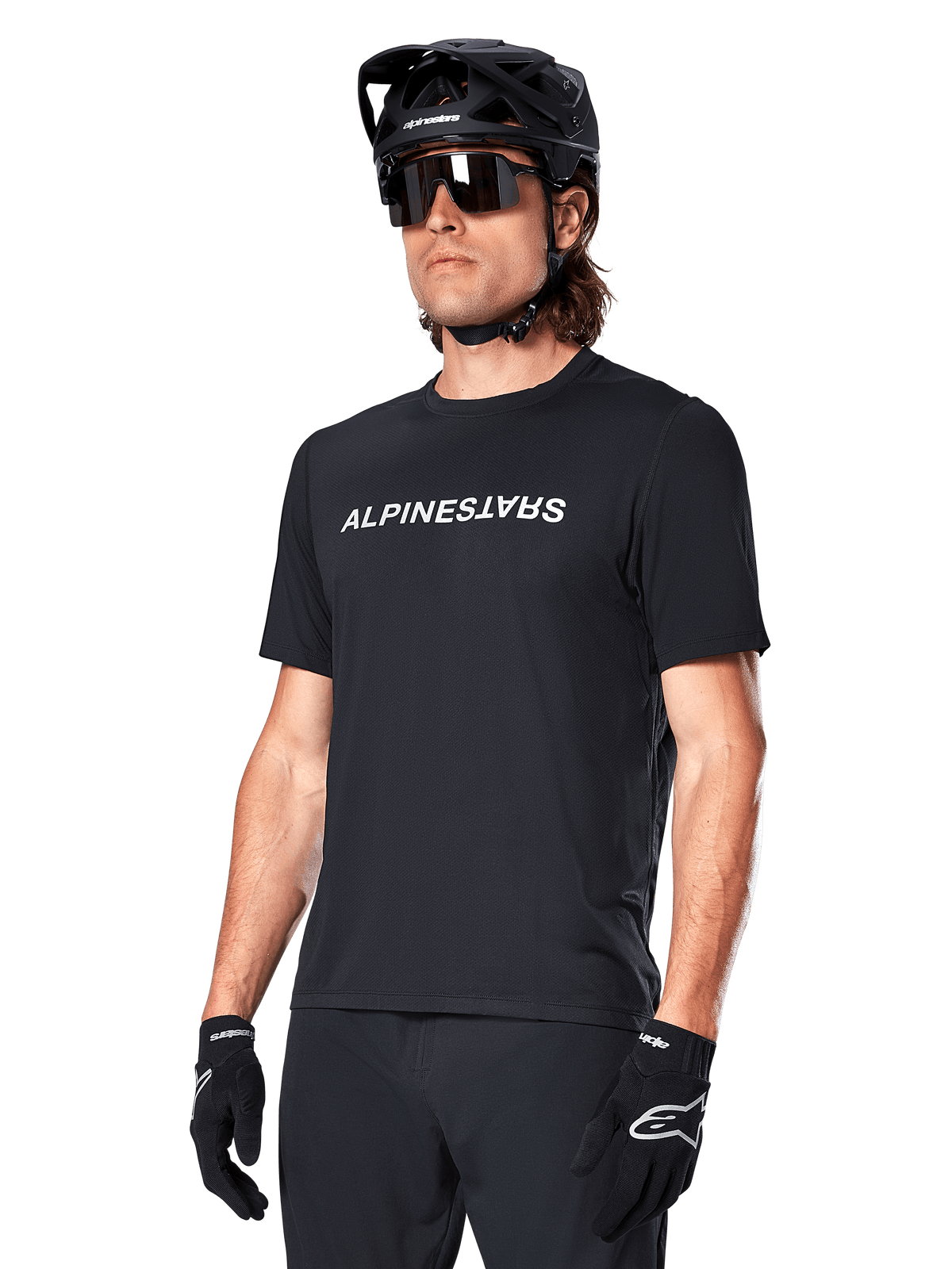 Alpinestars Maglia A-Dura Switch, maglia a maniche corte da MTB trail da uomo, nera, in tessuto tecnico con logo wordmark bianco sul petto, indossata con casco e occhiali da sole.
