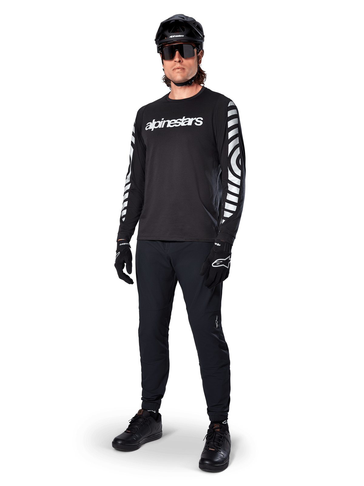 Maglia Alpinestars A-Dura Dri Oscar a maniche lunghe, Nero Riflettente, con scritta Alpinestars bianca sul petto e motivi grafici riflettenti sulle maniche, indossata con pantaloni da mountain bike neri, casco e guanti, abbigliamento tecnico da MTB