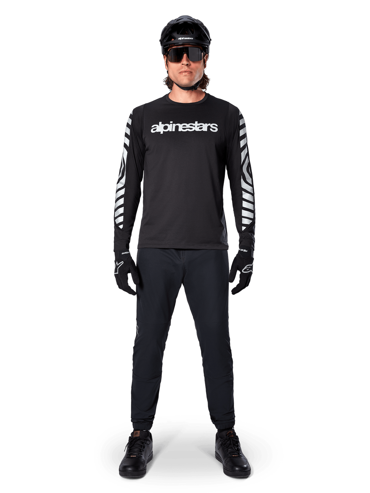 Maglia a maniche lunghe Alpinestars A-Dura Dri Oscar in nero riflettente, indossata con casco nero e occhiali da sole, con logo bianco sul petto e motivi grafici riflettenti sulle maniche, abbigliamento da MTB per guida off-road