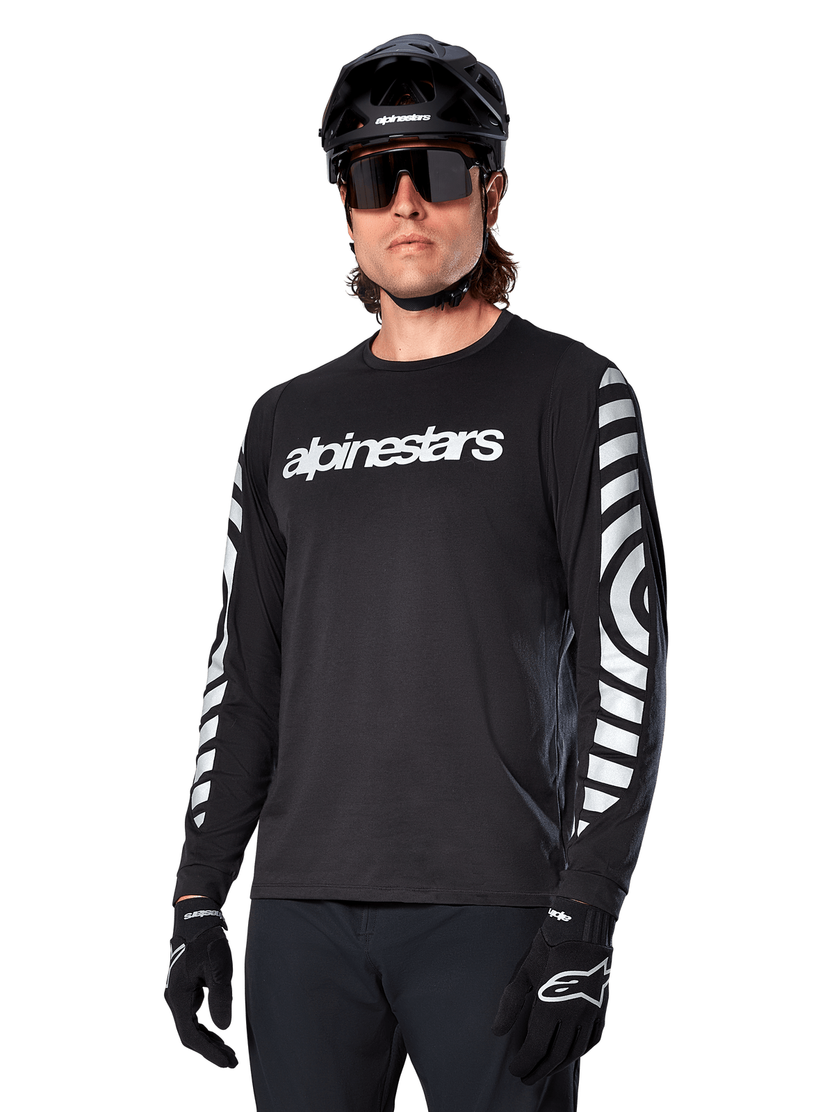 Alpinestars A-Dura Dri Oscar Jersey a maniche lunghe, maglia da ciclismo MTB, nero riflettente, con logo bianco sul petto e grafiche circolari riflettenti sulle maniche, indossata con casco nero e occhiali da sole, abbigliamento tecnico traspirante per mountain bike