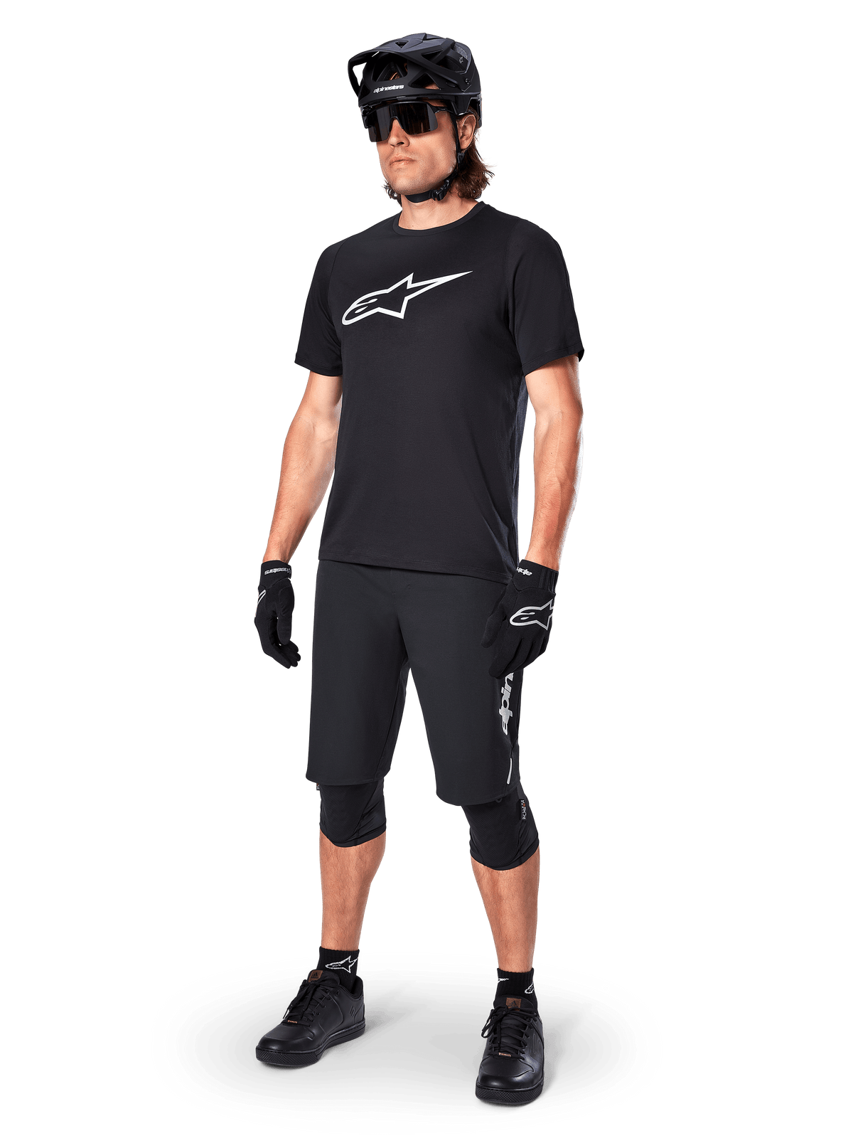 Ciclista di mountain bike che indossa la maglia a maniche corte Alpinestars A-Dura Dri Oscar in Black Reflective, con un grande logo bianco sul petto, abbinata a pantaloncini MTB, guanti e casco neri coordinati, abbigliamento tecnico da ciclismo per prestazioni fuoristrada