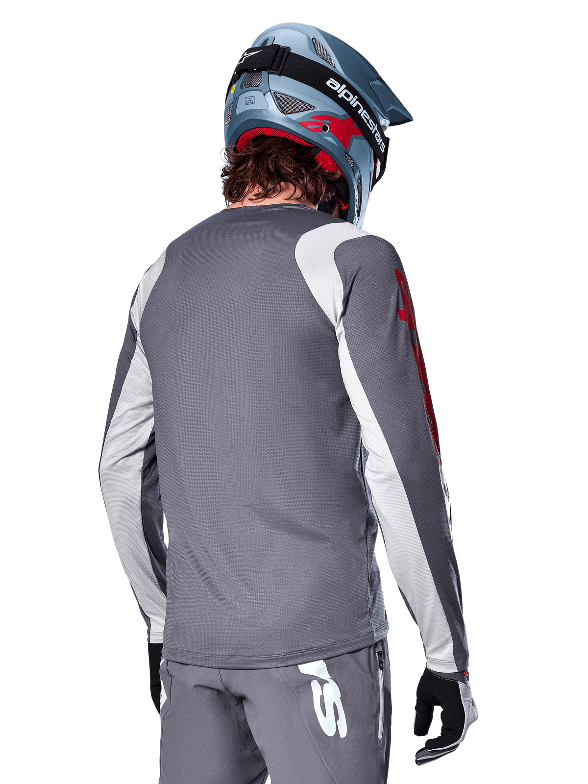 Alpinestars Maglia a maniche lunghe A-Supra Astar, grigio scuro con pannelli grigio chiaro su spalle e braccia, vista posteriore di un pilota con casco integrale da mountain bike blu e pantaloni grigi, abbigliamento da ciclismo MTB con vestibilità performante