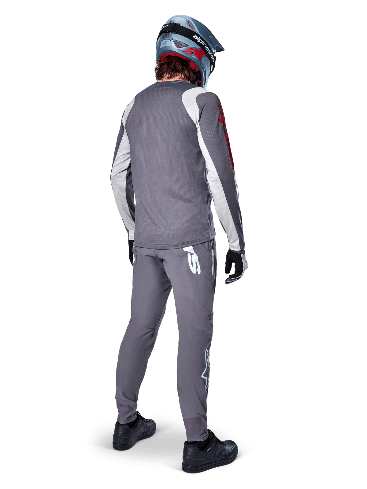 Alpinestars A-Supra Astar Jersey, maglia da MTB a maniche lunghe, grigio scuro con dettagli bianchi sulle maniche e logo rosso, vista posteriore del rider con pantaloni grigi abbinati e casco integrale blu, abbigliamento tecnico da ciclismo