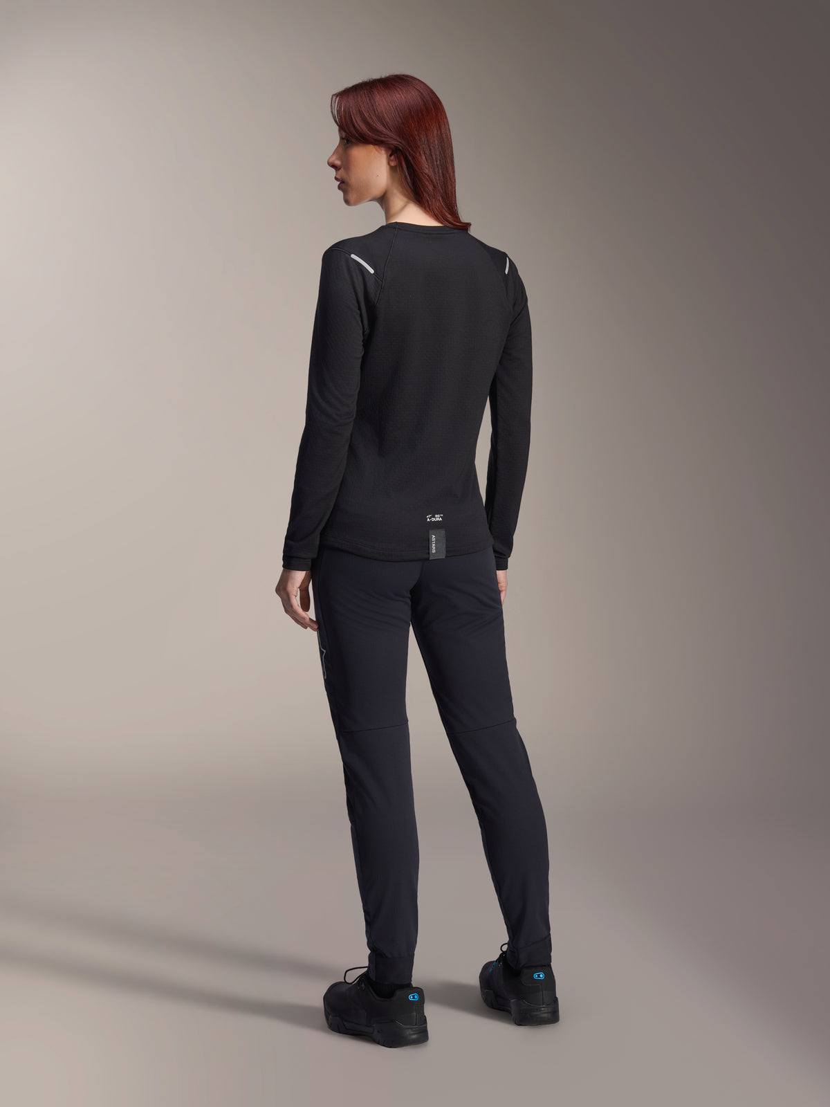 Alpinestars Stella A-Dura Thermal Jersey da donna, maglia da MTB a maniche lunghe in nero, vista posteriore con dettagli riflettenti sulle spalle e coda allungata, indossata con pantaloni e scarpe neri, abbigliamento tecnico per mountain bike