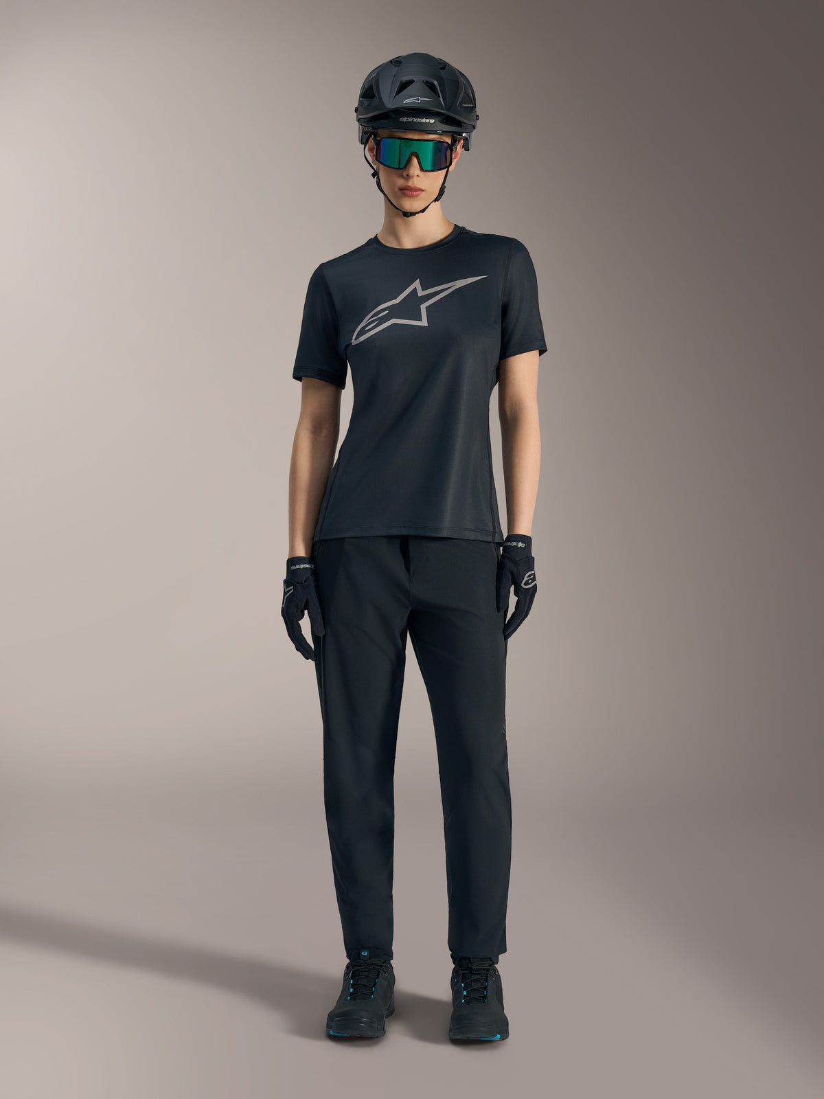 Maglia Stella A-Dura Ride SS da donna nera con logo argento, abbinata a pantaloni e casco MTB per guida fuoristrada.
