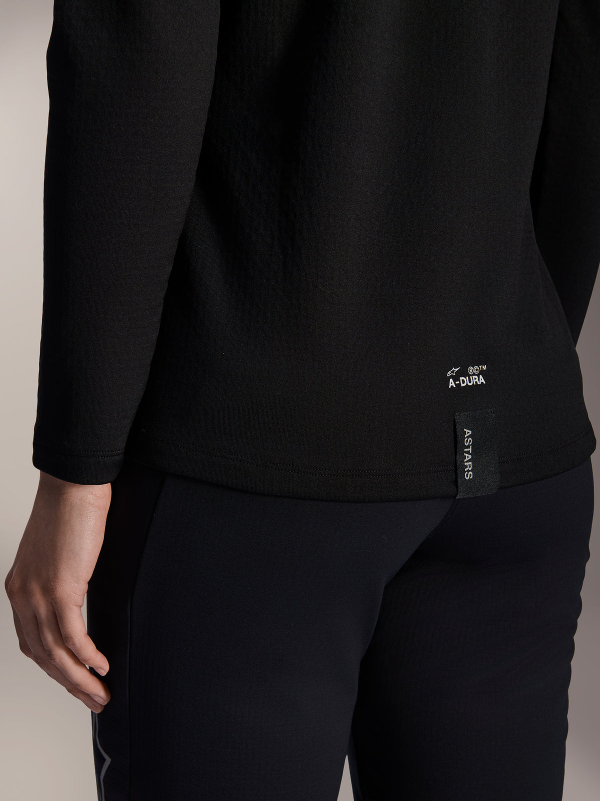 Alpinestars Stella A-Dura Thermal Jersey da donna, maglia termica da MTB nera, primo piano del bordo inferiore posteriore con branding A-DURA bianco ed etichetta logo ASTARS verticale, abbigliamento per mountain bike in climi freddi