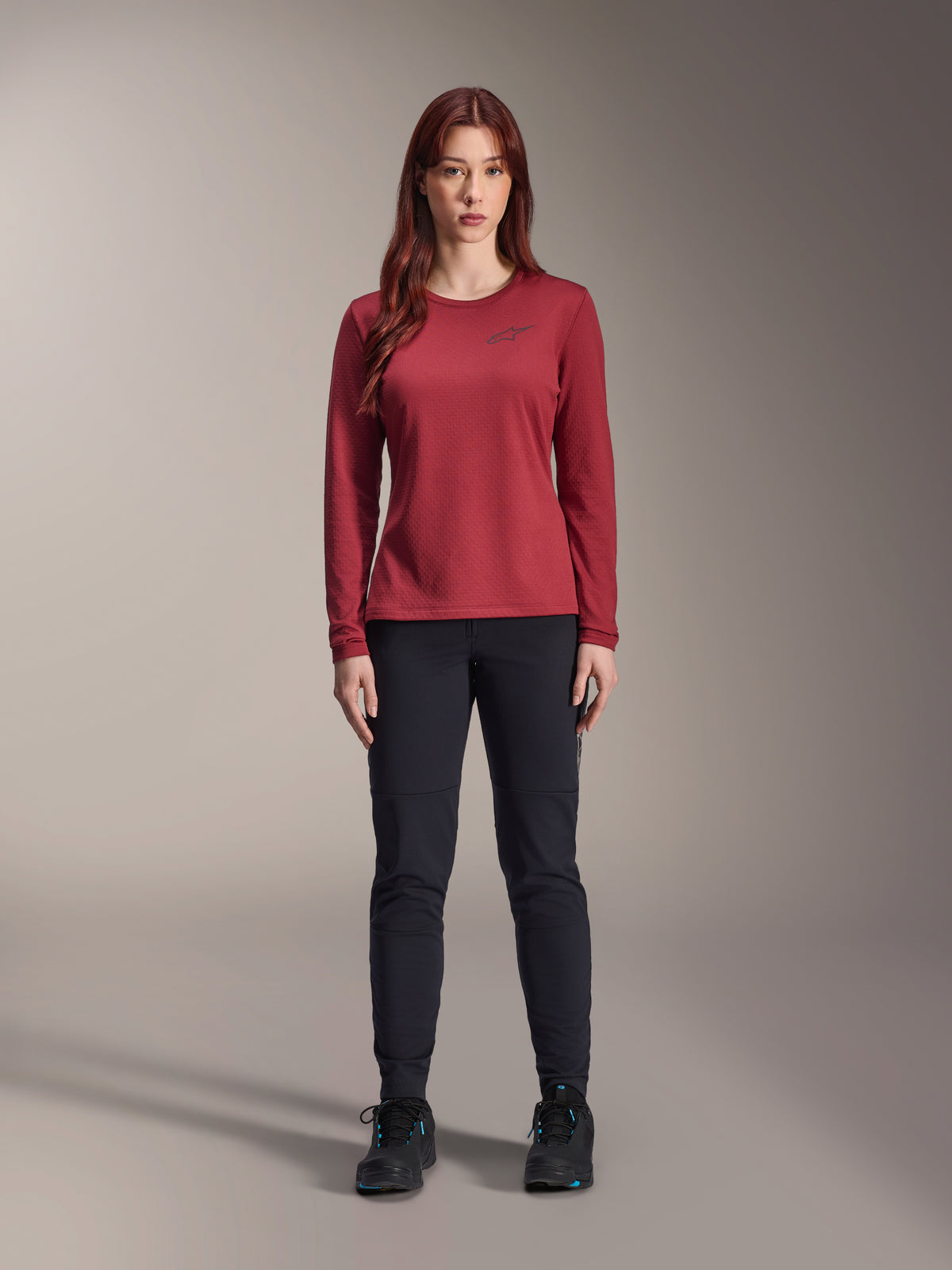 Alpinestars Maglia Termica Donna Stella A-Dura, maglia da ciclismo a maniche lunghe, bordeaux, indossata da una modella con pantaloni neri e scarpe nere, presenta un logo discreto sul petto, vestibilità regolare per mountain bike