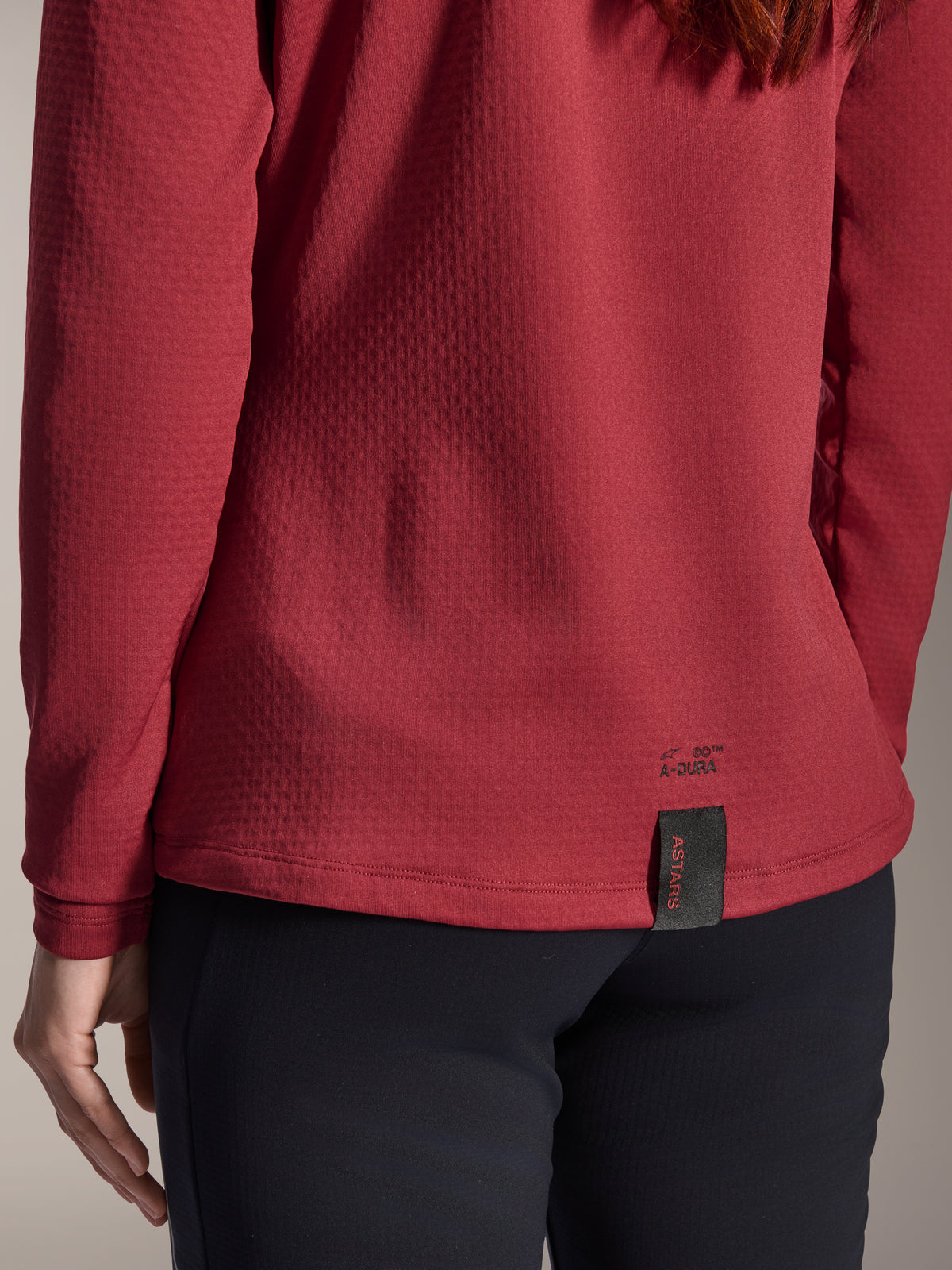 Maglia termica Alpinestars Stella A-Dura da donna, bordeaux, vista ravvicinata dell'orlo posteriore con marchio A-Dura ed etichetta tessuta ASTARS, tessuto in pile isolante testurizzato, abbigliamento da mountain bike da donna
