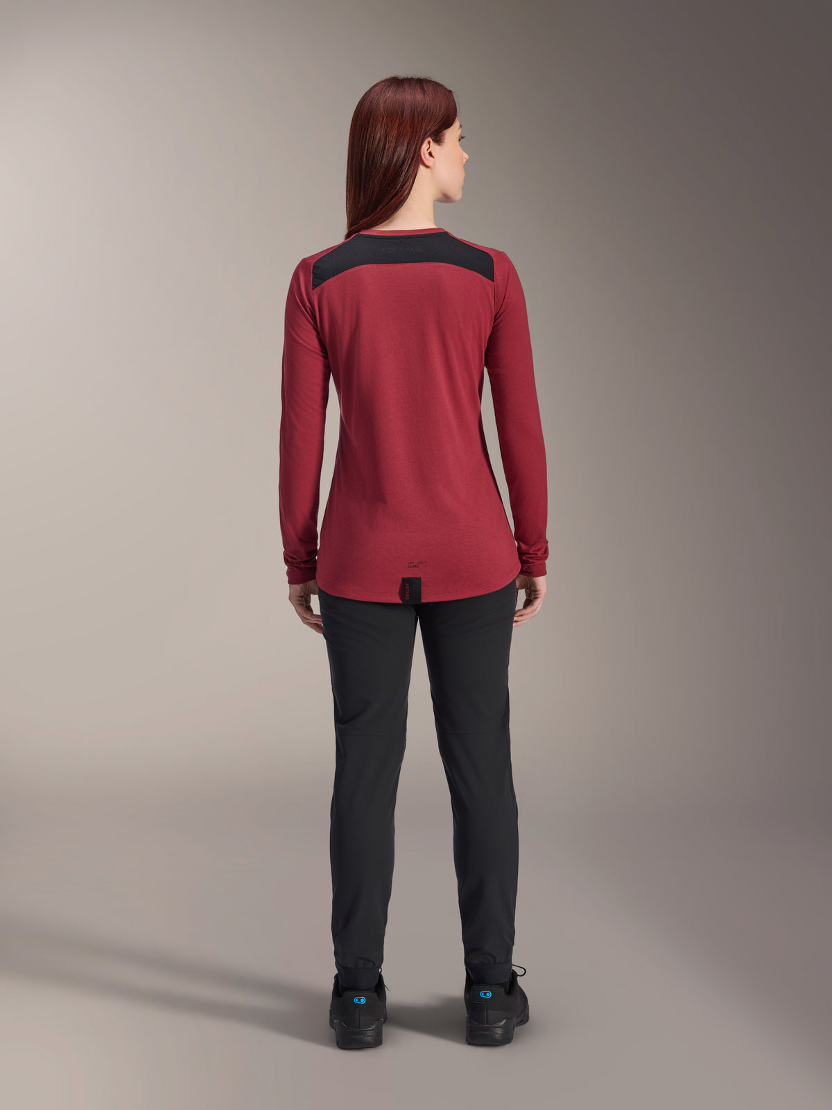 Maglia Alpinestars Stella A-Dura Dri Astar Long Sleeve da donna, rosso borgogna con pannelli in mesh nero sulle spalle, abbigliamento tecnico da MTB visto dal retro con pantaloni neri, design con coda lunga per maggiore copertura durante il ciclismo