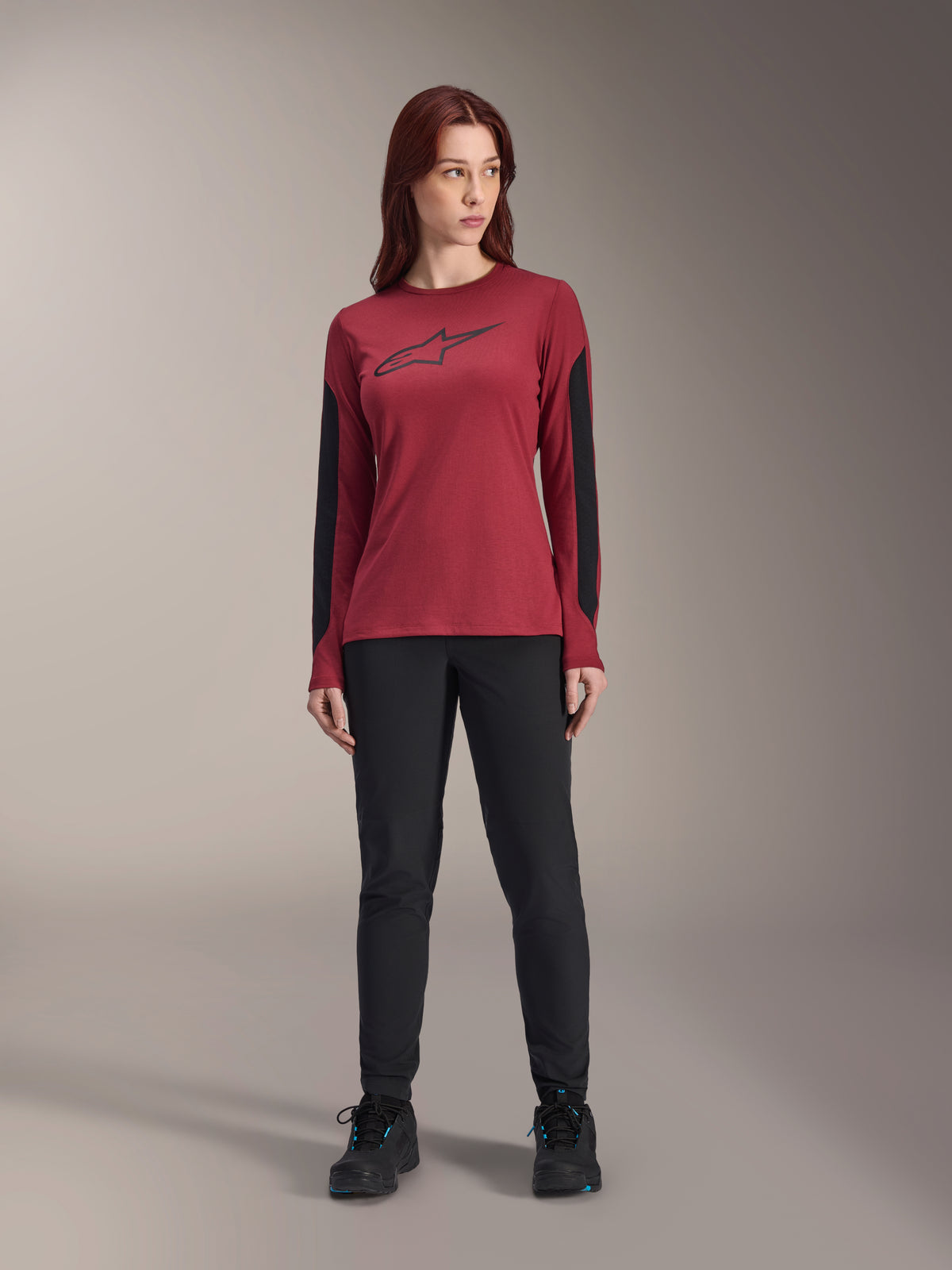 Maglia a maniche lunghe da donna Alpinestars Stella A-Dura Dri Astar in bordeaux, con logo Astars nero sul petto e pannelli in mesh nero sulle braccia, abbinata a pantaloni tecnici neri e scarpe sportive, abbigliamento performance da mountain bike per donna