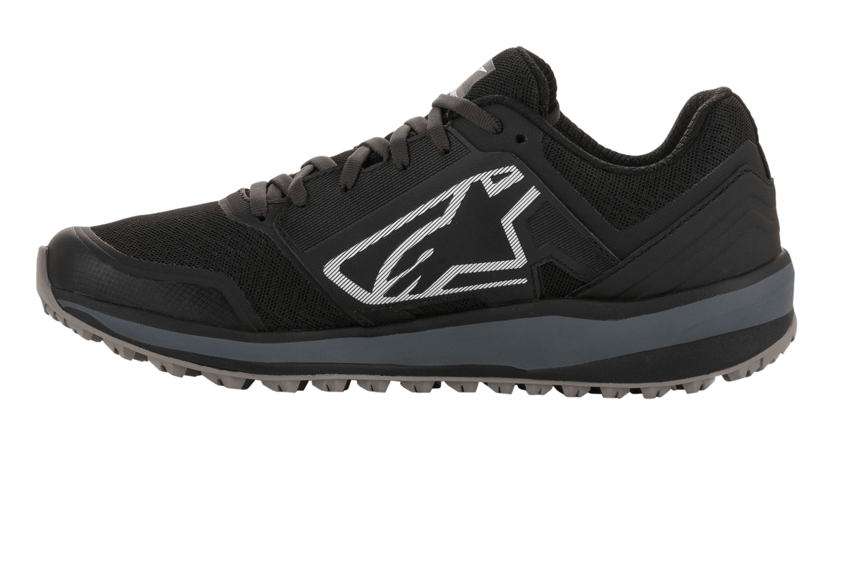 Alpinestars Meta Trail Shoes, scarpa da running performante, nero e grigio scuro, profilo laterale con grande logo Astars bianco, intersuola grigio scuro e suola in gomma tassellata resistente all'olio, progettata per il comfort nel paddock e l'uso da parte dei team motorsport