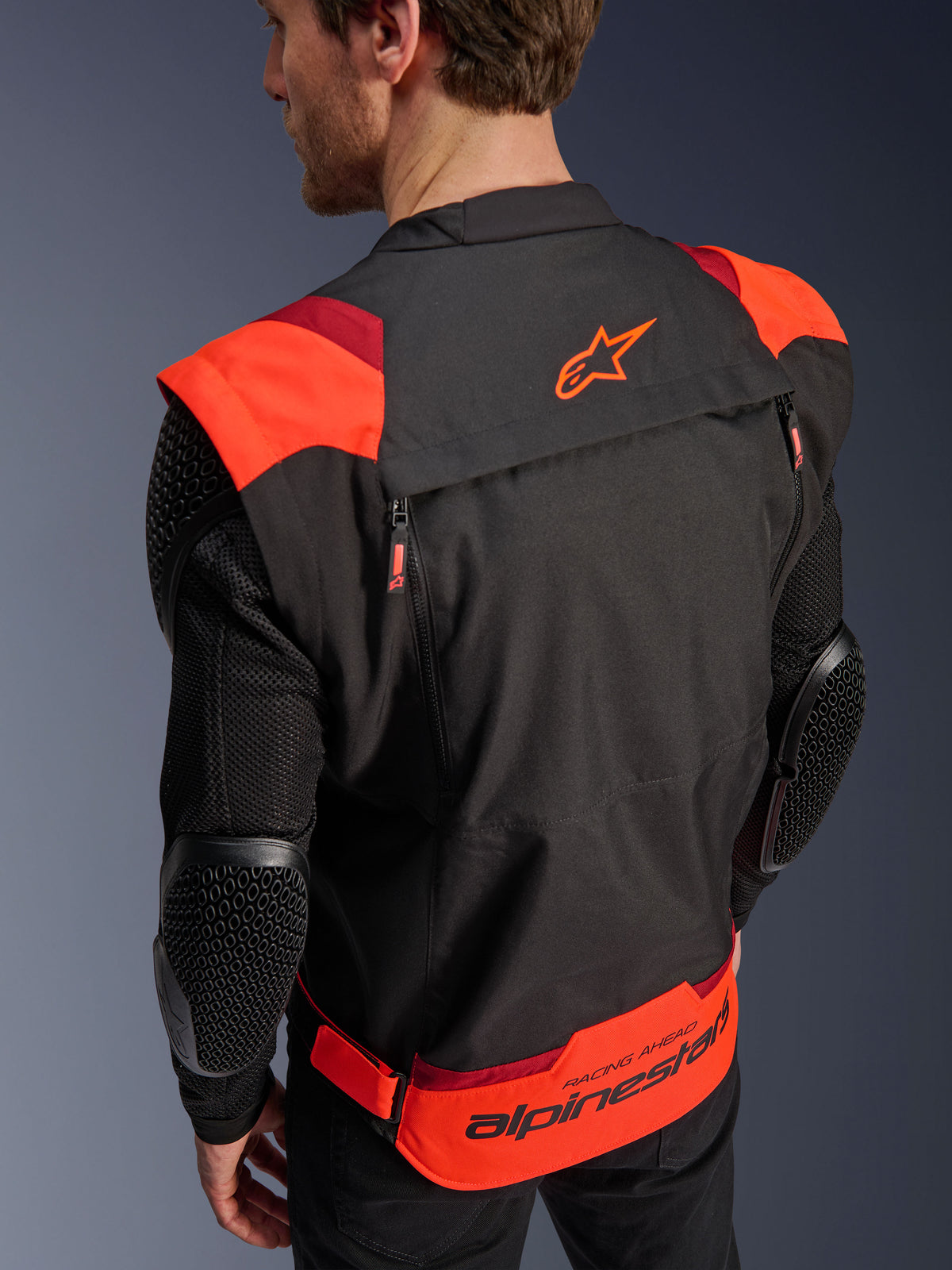 Giacca Alpinestars T-Stunt Air, nero, rosso fluo e rosso scuro, vista posteriore su un modello, mostra maniche in rete con protezioni per i gomiti con texture a nido d'ape, logo a stella Alpinestars sulla parte superiore della schiena e branding 'RACING AHEAD' sulla parte inferiore, design modulare a taglio sportivo per moto.
