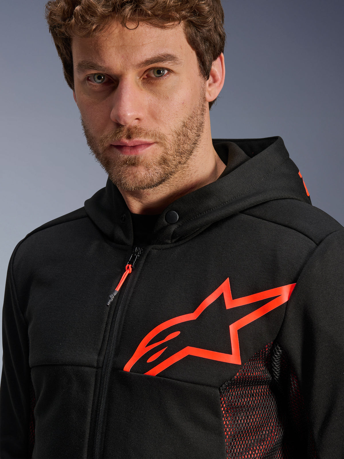 Alpinestars Chrome Air Sport Hoodie, nero e rosso fluo, primo piano che mostra il grande logo a stella rosso fluo sul petto, pannelli laterali in rete rossa per la ventilazione, cerniera frontale e colletto con bottone a pressione, abbigliamento moto urban casual