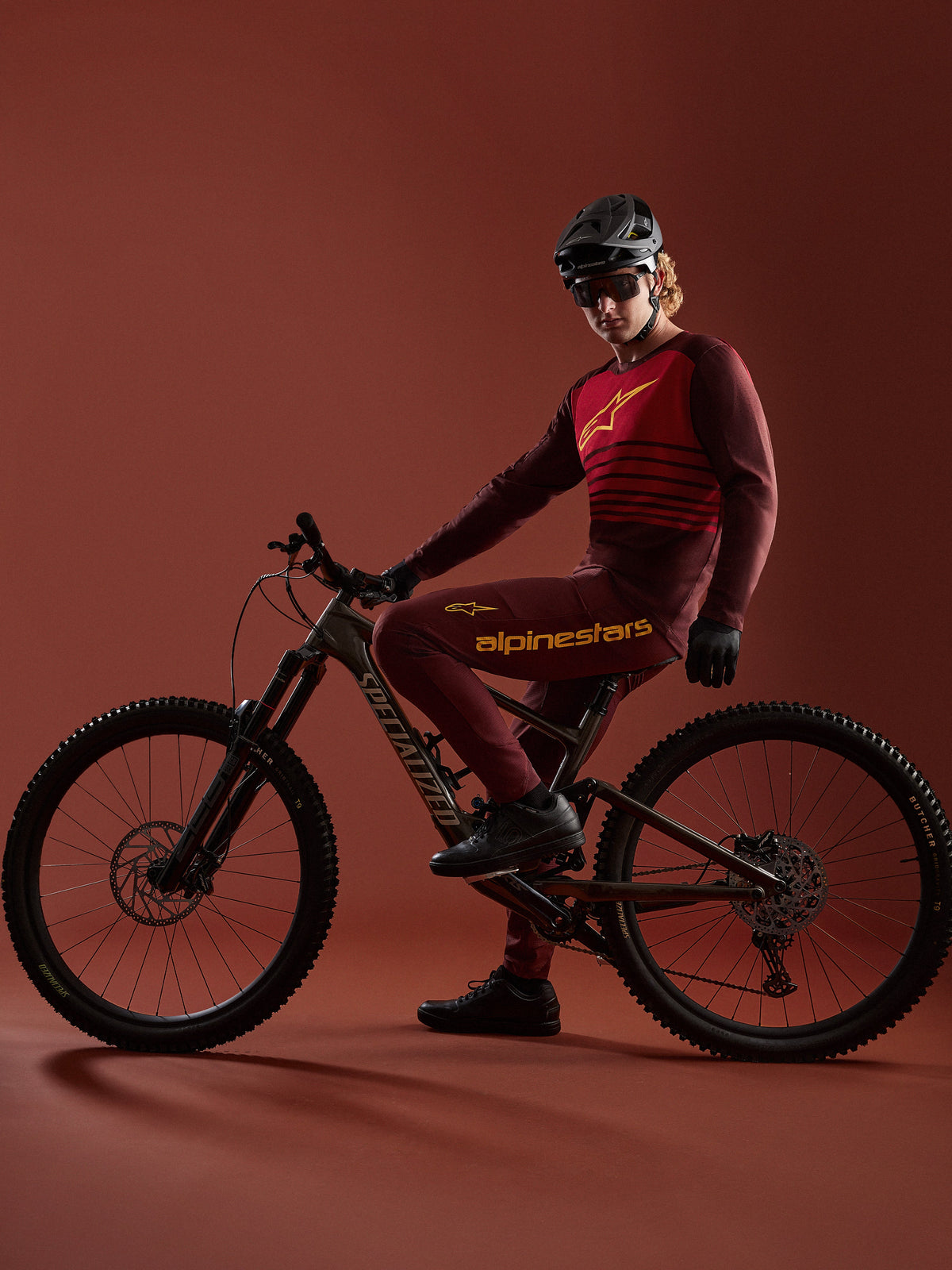 Kit Alpinestars A-Dura Elite 2.0 bordeaux con maglia e pantaloni coordinati e bici Specialized in studio.