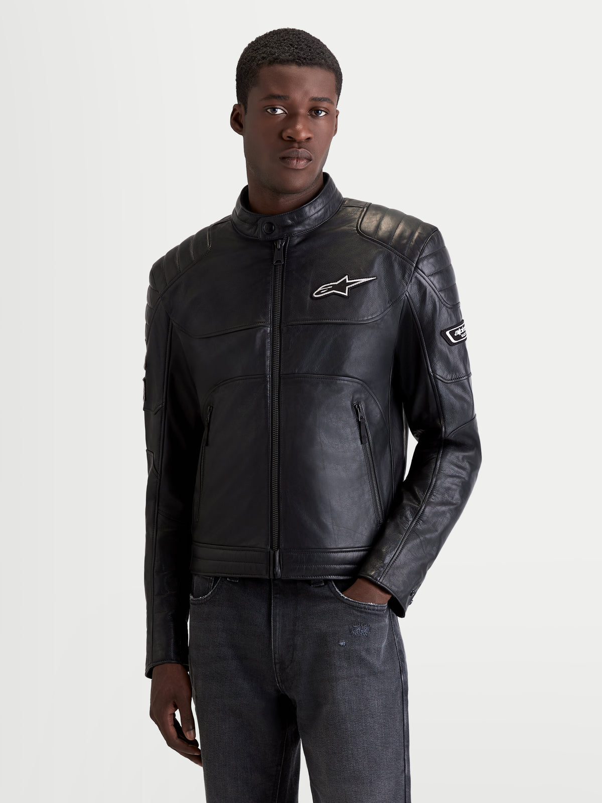 Alpinestars Revern Giacca di pelle, giacca da moto urbana da uomo in pelle nera, vista frontale su un modello che indossa abbigliamento heritage con protezioni certificate per spalle e gomiti