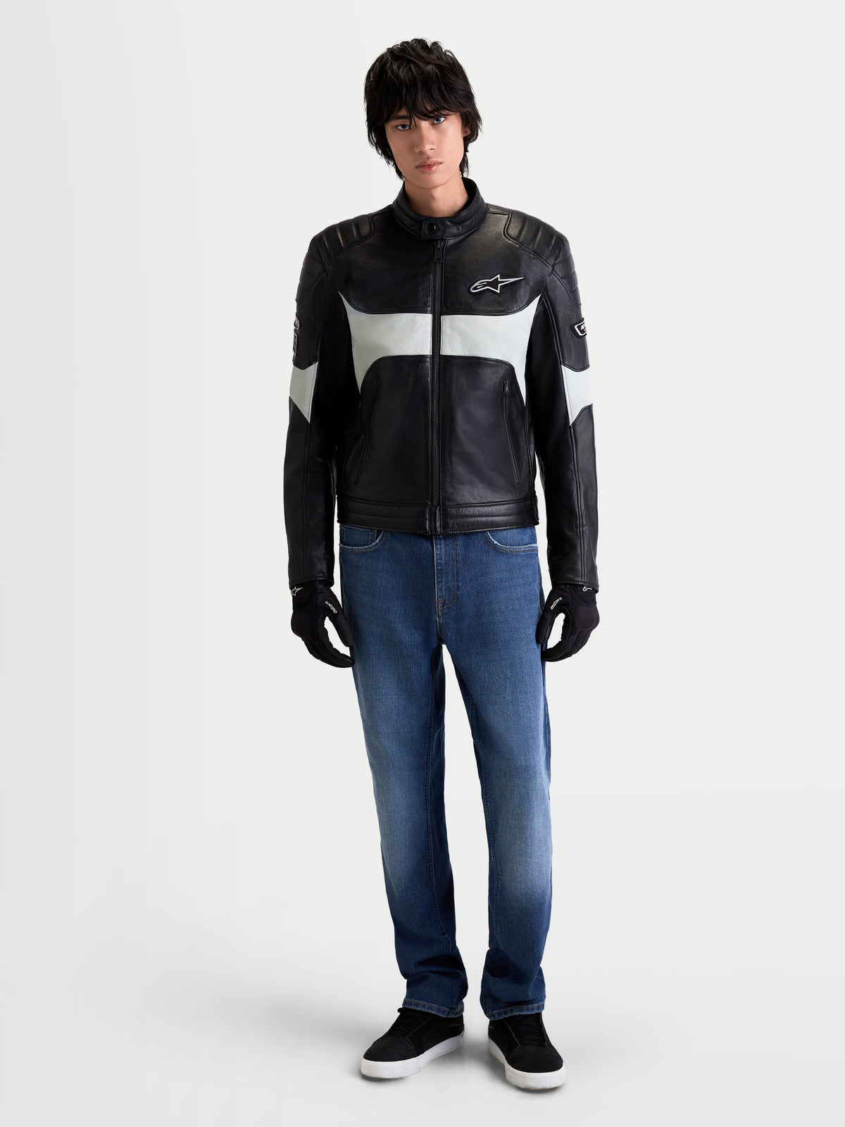 Alpinestars Revern Giacca di pelle, giacca da moto urbana da uomo in pelle nera e grigio metallizzato, vista frontale su un modello che indossa jeans e guanti neri, con dettagli heritage e struttura in pelle bovina pieno fiore
