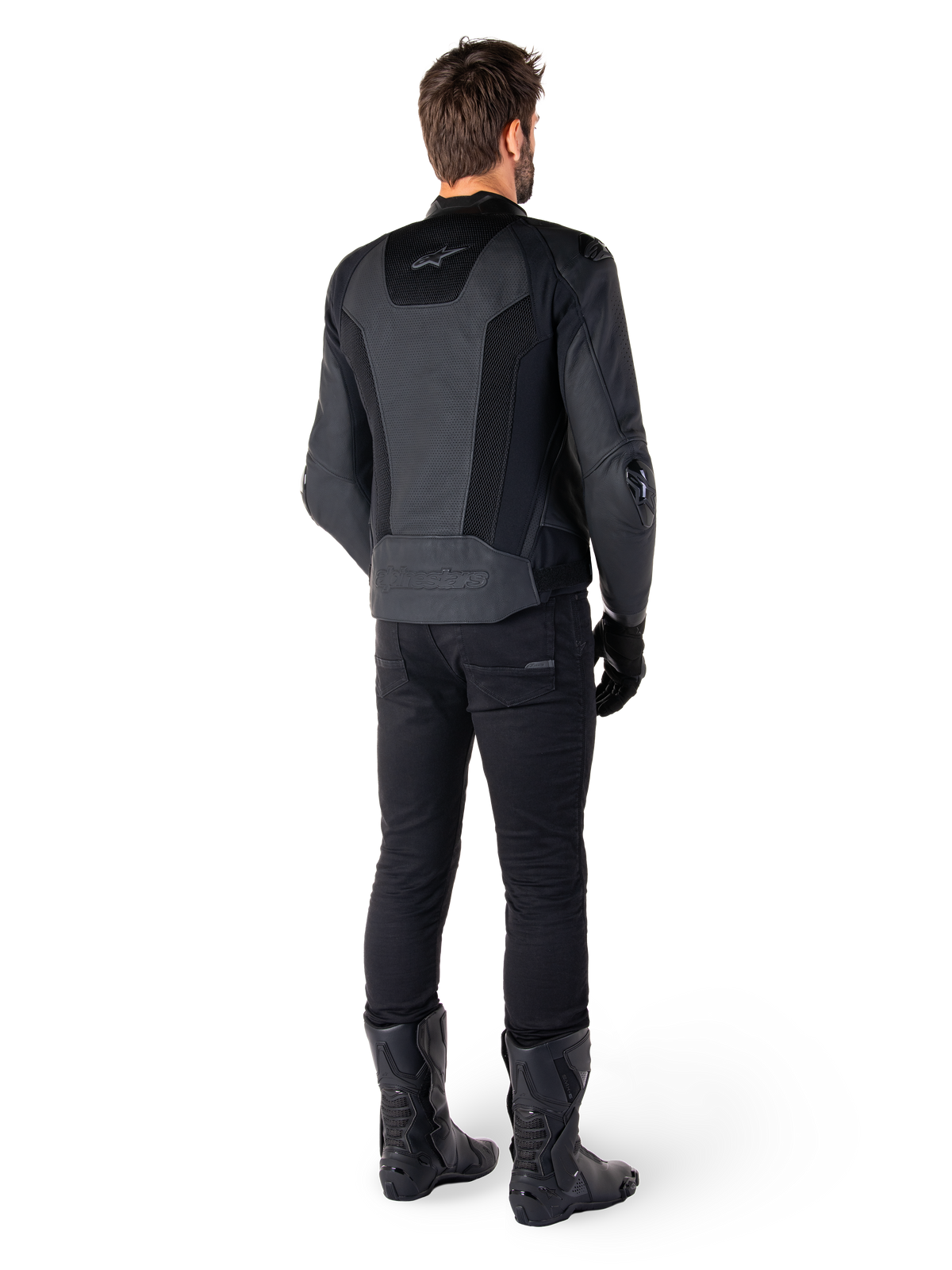 Vista posteriore di un uomo che indossa la giacca in pelle Alpinestars Missile V3 Airflow in nero, dotata di ampi pannelli traforati per la ventilazione, abbinata a pantaloni da moto e stivali neri, che mette in mostra un'estetica racing aerodinamica.