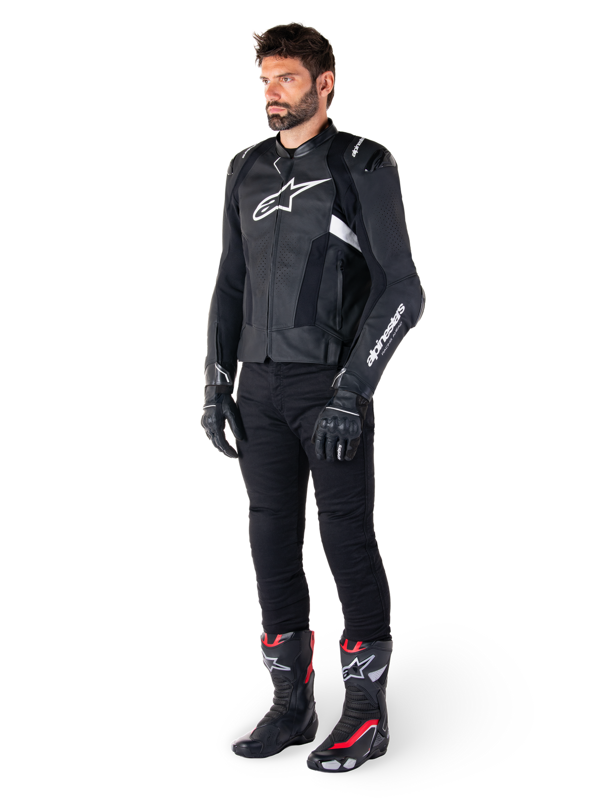 Giacca in pelle Alpinestars Missile V3 Airflow, nero e bianco, indossata da un modello con pantaloni da moto neri, guanti neri e stivali da corsa con accenti rossi e bianchi, con pelle traforata e loghi bianchi, abbigliamento tecnico da moto racing
