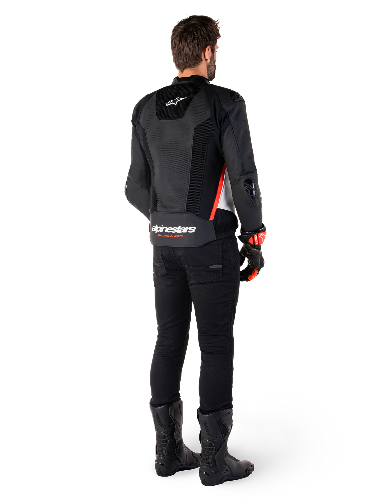 Pilota visto di spalle che indossa la giacca in pelle Alpinestars Missile V3 Airflow in Nero Bianco Rosso Fluo, abbinata a pantaloni neri e stivali neri, con ampie zone in pelle traforata per la ventilazione, protezioni DFS sulle spalle e logo Alpinestars in evidenza sulla parte bassa della schiena.