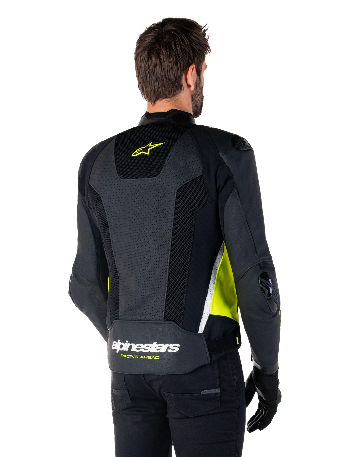 Alpinestars Missile V3 Airflow Leather Jacket, vista posteriore su un modello, nero con accenti giallo fluorescente e bianco, ampi pannelli in pelle traforata e mesh sulla schiena, logo a stella giallo e scritta 'RACING AHEAD' bianca, abbinata a guanti e pantaloni neri.