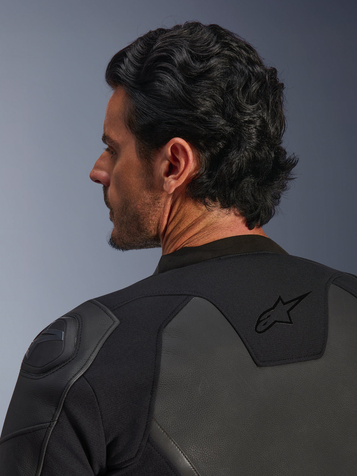 Giacca in pelle Alpinestars GP Force V2, nero, inquadratura ravvicinata da dietro, con logo a stella nero sulla parte superiore della schiena e protezione spalla GP Lite Evo DFS, costruzione multi-pannello in pelle e tessuto, vista in studio del profilo del pilota e dettagli dell'attrezzatura.