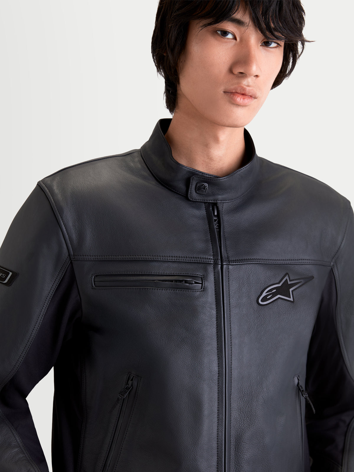 Alpinestars Maver X Giacca di pelle, giacca da moto urbana contemporanea da uomo, colore nero, vista ravvicinata frontale su un modello che indossa una giacca in pelle bovina di prima qualità con tasche con cerniera e colletto da motociclista