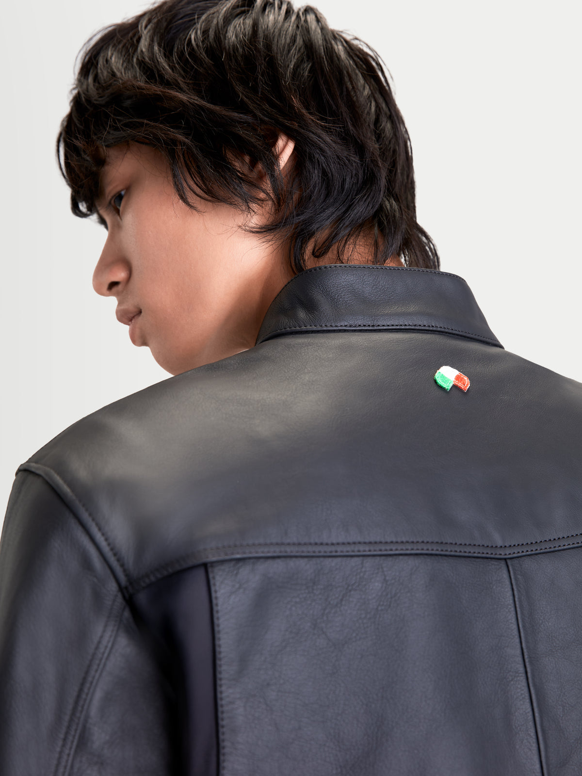 Alpinestars Maver X Giacca di pelle, giacca da moto urban da uomo in pelle nera, vista posteriore ravvicinata che mostra la costruzione in pregiata pelle bovina, il collo alla coreana e il dettaglio della bandiera italiana indossata da un modello