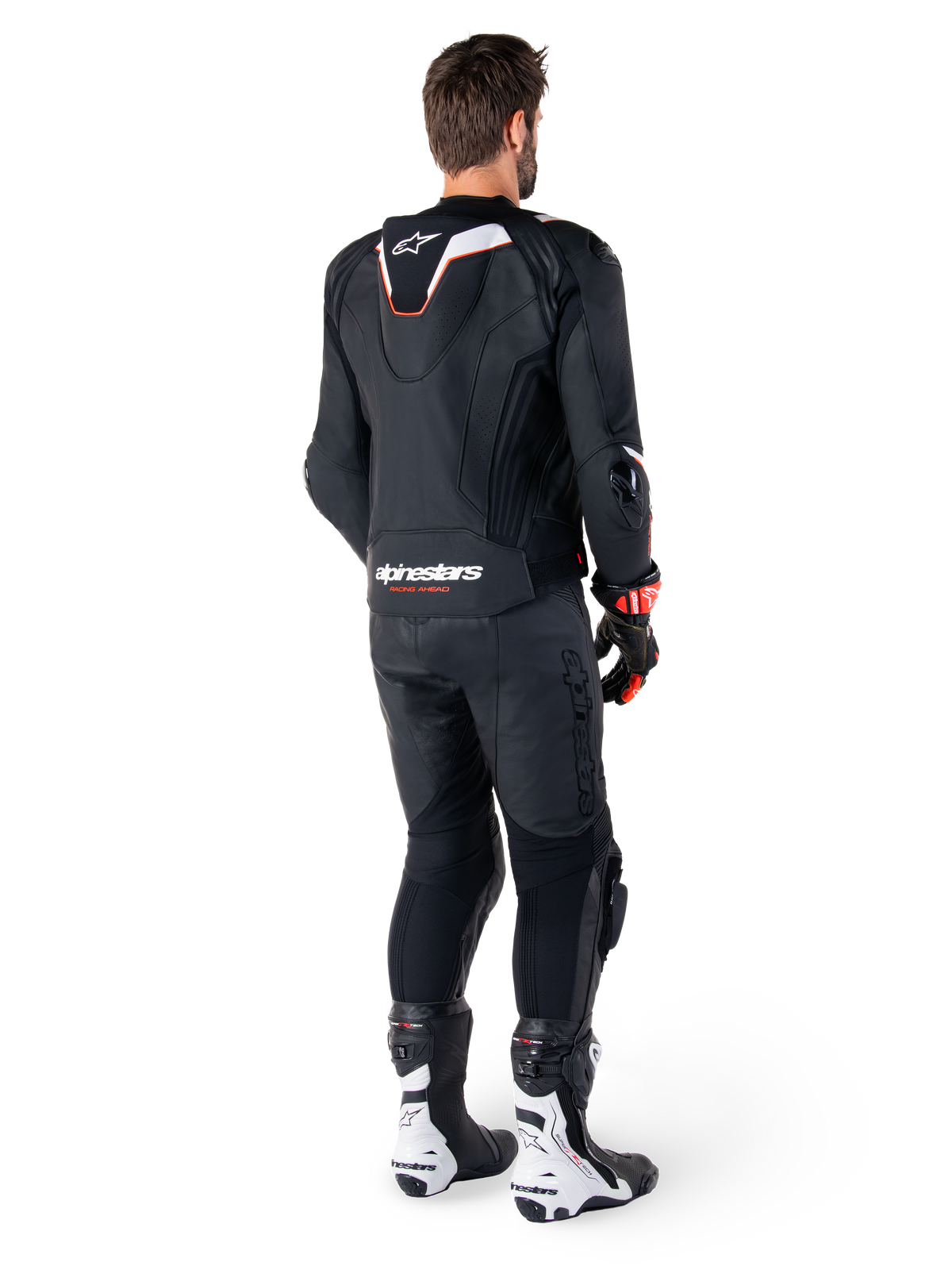 Vista posteriore di un pilota che indossa la giacca in pelle Alpinestars Missile V3 Ignition in nero, con gobba aerodinamica sportiva sottile con accenti bianchi e rossi, marchio Alpinestars sulla parte bassa della schiena, abbinata a pantaloni in pelle neri coordinati e stivali da corsa bianchi e neri, completo sportivo professionale da moto