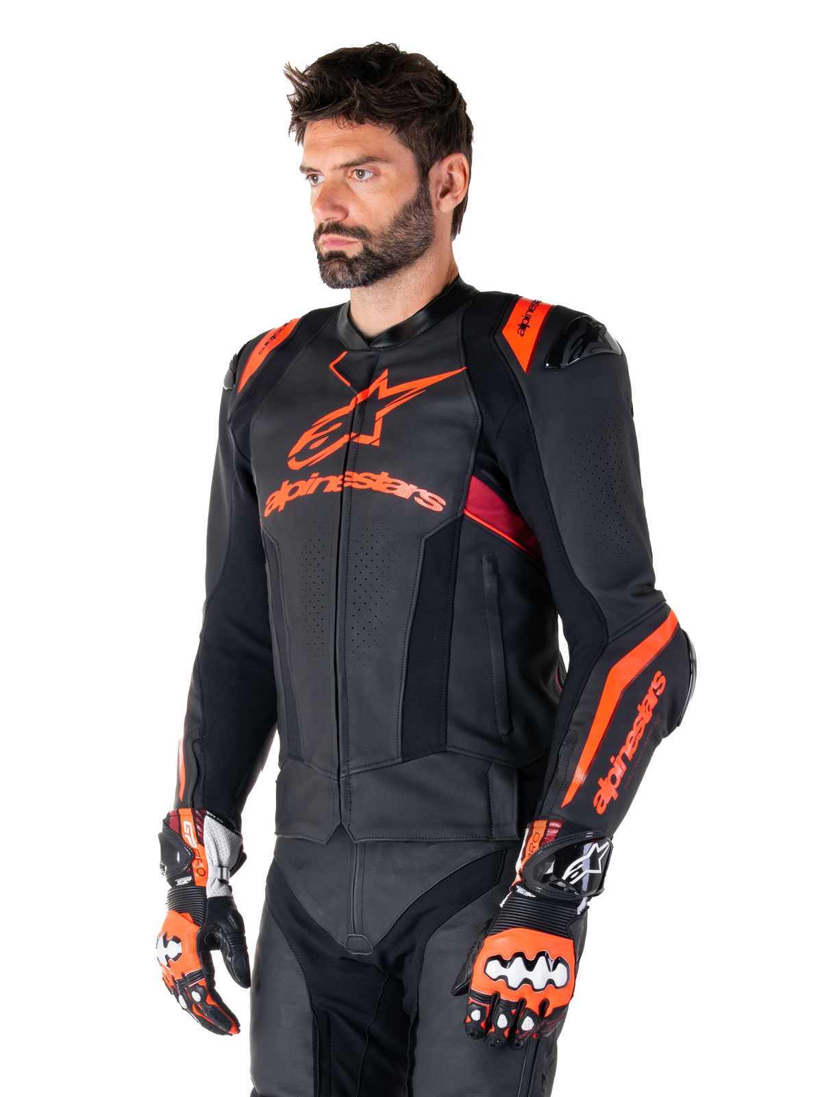 Giacca in pelle Alpinestars Missile V3 Ignition, nero con accenti rosso fluo e rosso scuro, indossata da un modello uomo con guanti da corsa e pantaloni in pelle abbinati, con logo Alpinestars evidente, pannelli in pelle traforata e protezioni esterne per le spalle, abbigliamento professionale da gara motociclistica