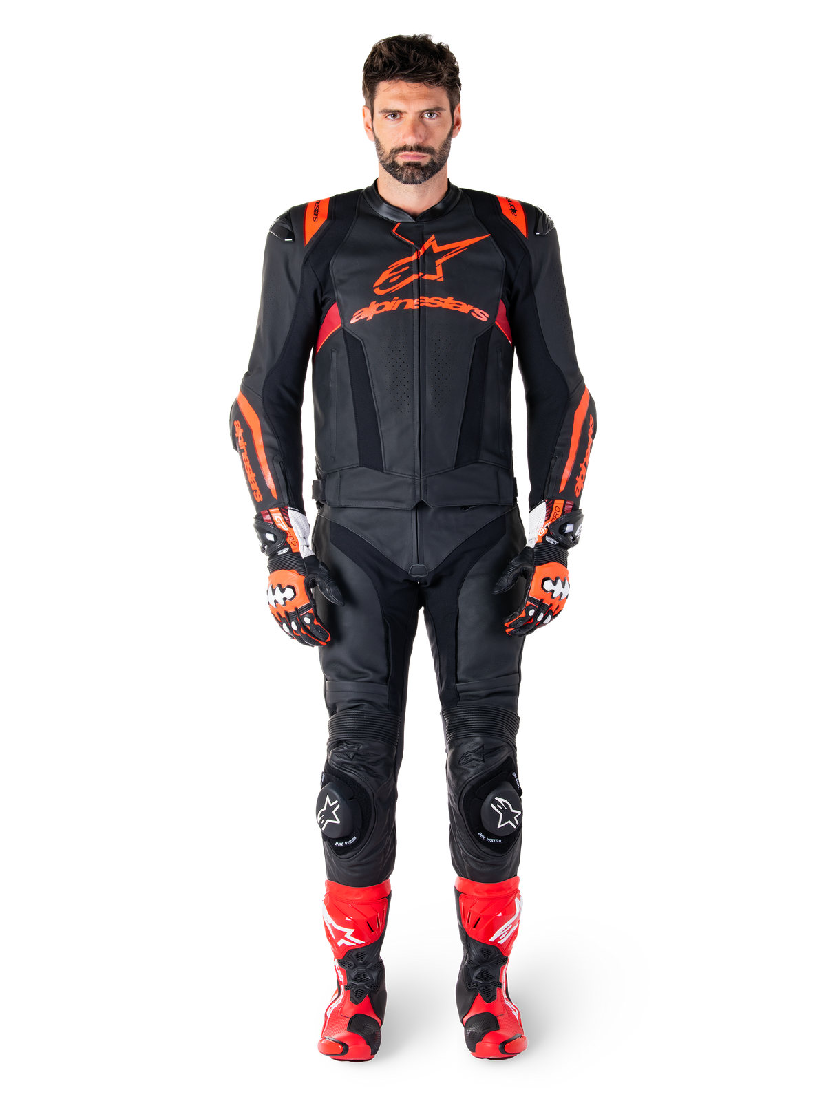 Modello maschile che indossa la giacca in pelle Alpinestars Missile V3 Ignition in Nero Rosso Fluo Rosso Scuro, equipaggiamento completo da gara motociclistica con pantaloni in pelle coordinati, guanti da corsa e stivali, caratterizzato dal logo Alpinestars sul petto, posa frontale, abbigliamento professionale per guida sportiva